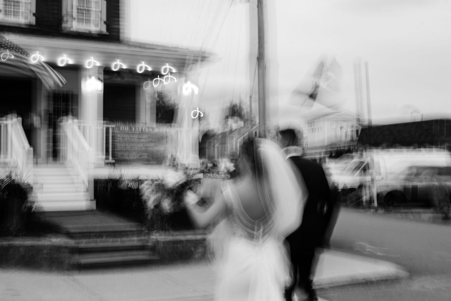 Artistic blurred black and white photo of couple dancing outside venue with string lights.