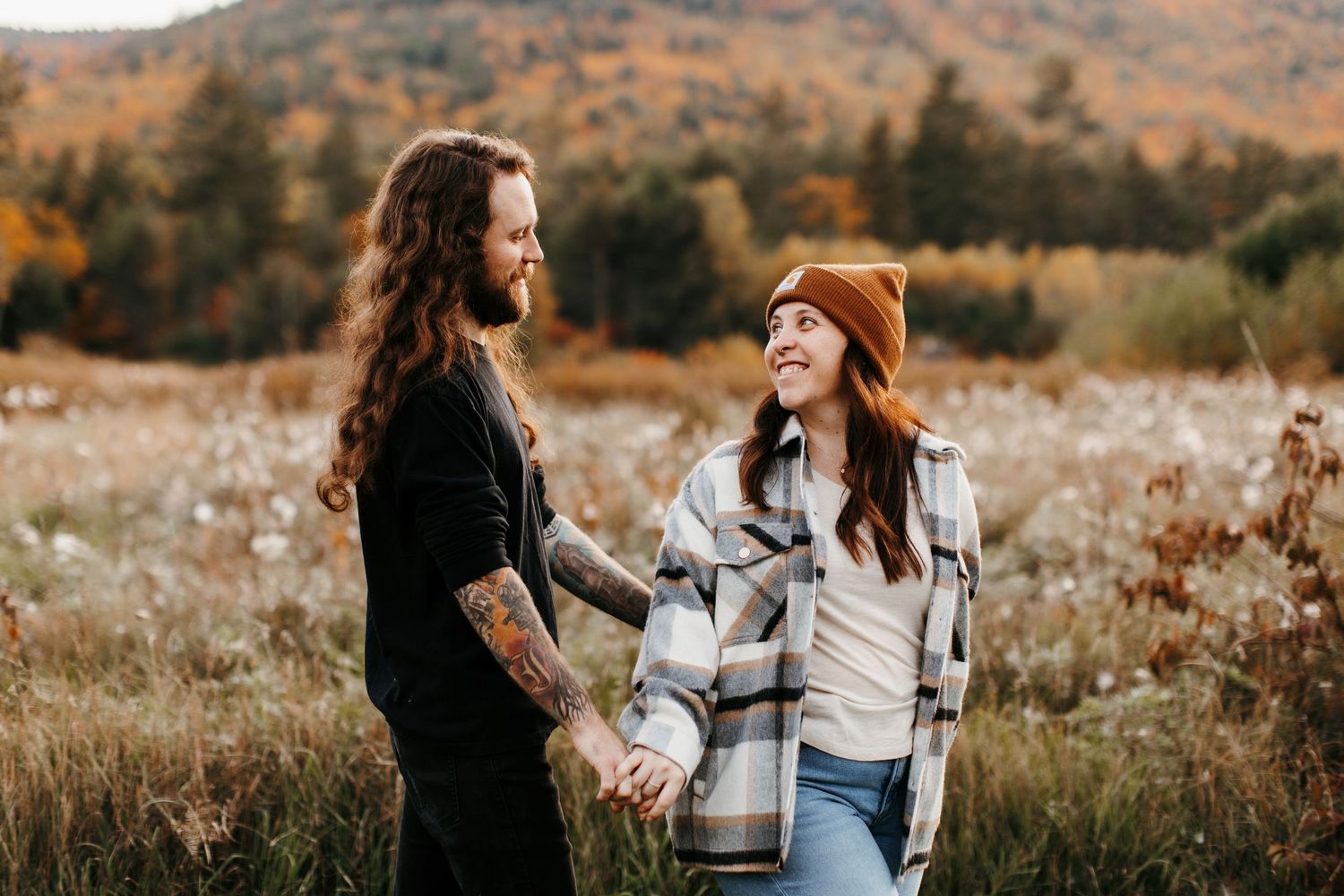 Two people share a laugh while standing in a golden autumn field at sunset.