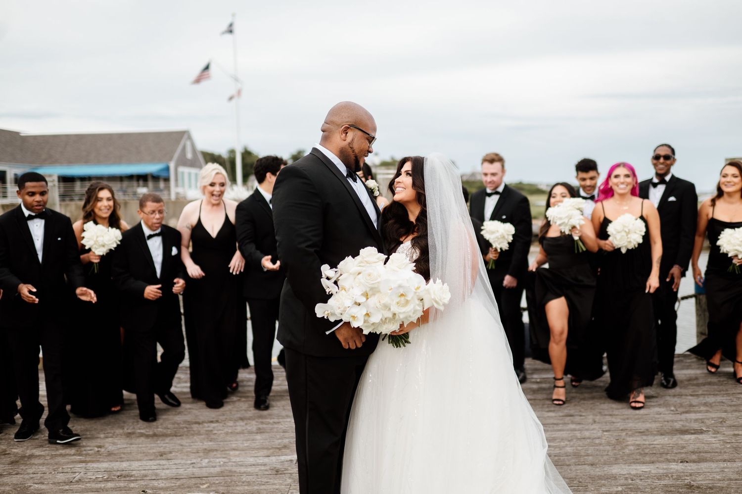 A wedding party celebrates with joy and laughter during an outdoor reception by the water.