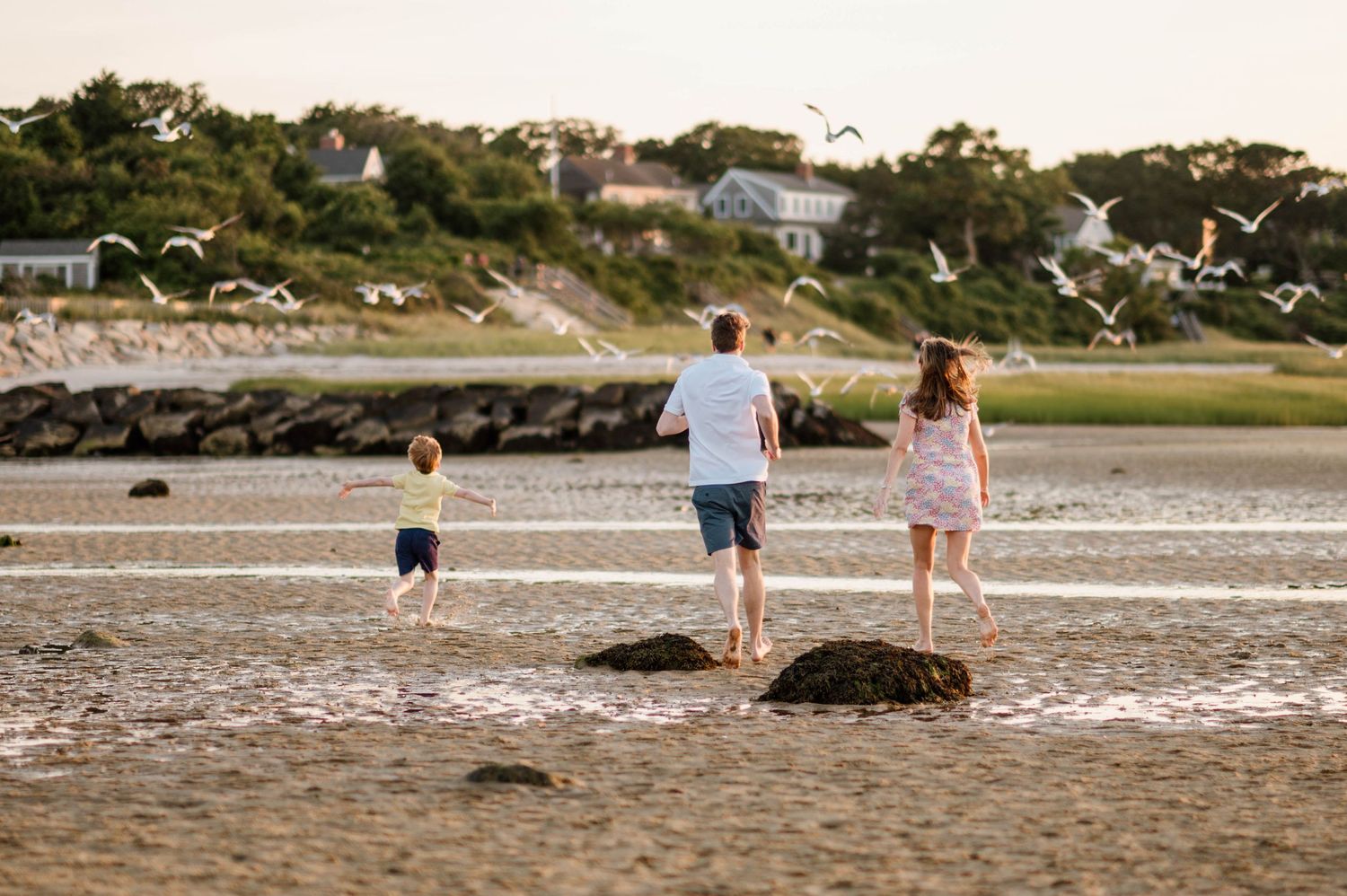 Family walks together on sandy beach at sunset with rocks and ocean in background.