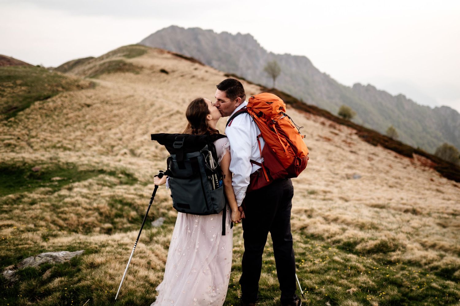 Couple in wedding attire embracing on a scenic mountain ridge with dramatic cloudy skies in the background.
