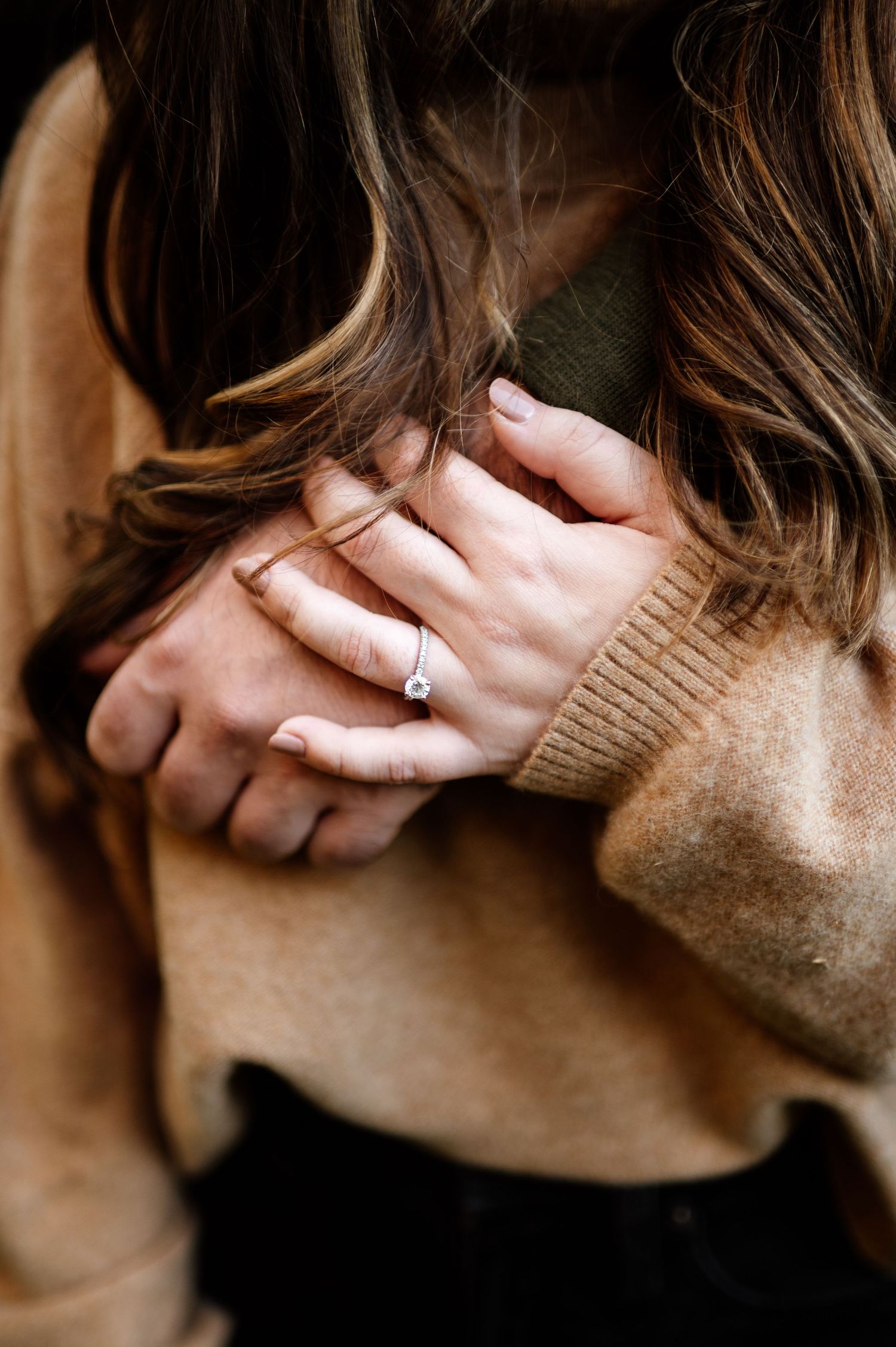Close-up artistic portrait showing hands gently caressing face with engagement ring visible.