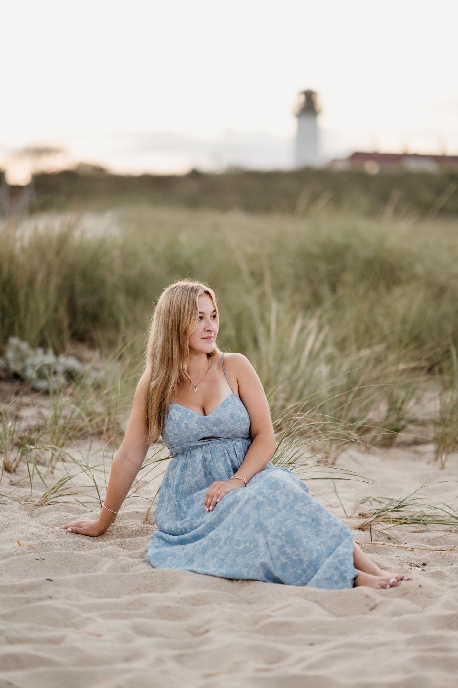 A woman in a light blue floral dress poses gracefully on a sandy beach during golden hour.