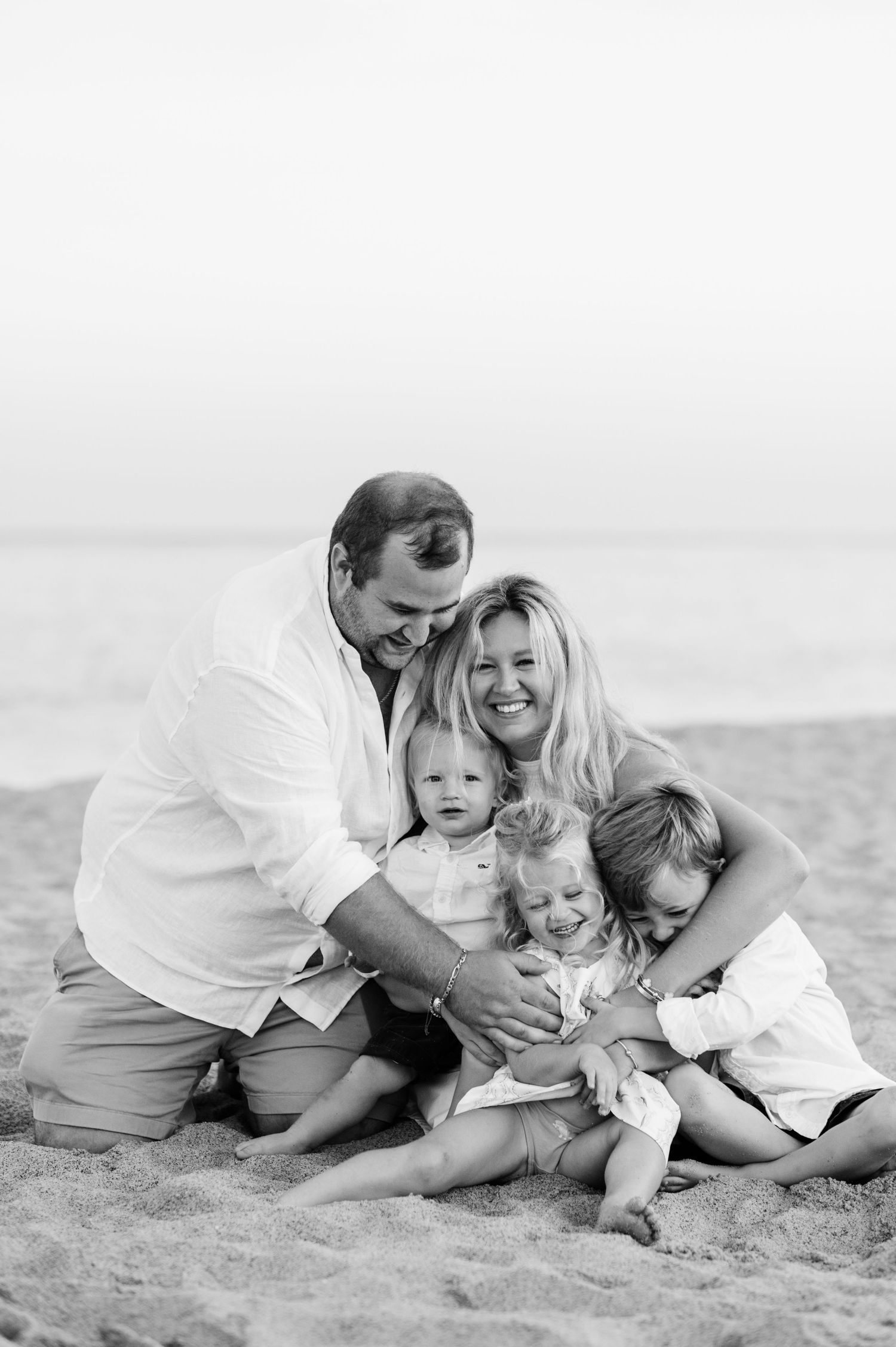 A family shares tender moments while lying together on a white sandy beach.