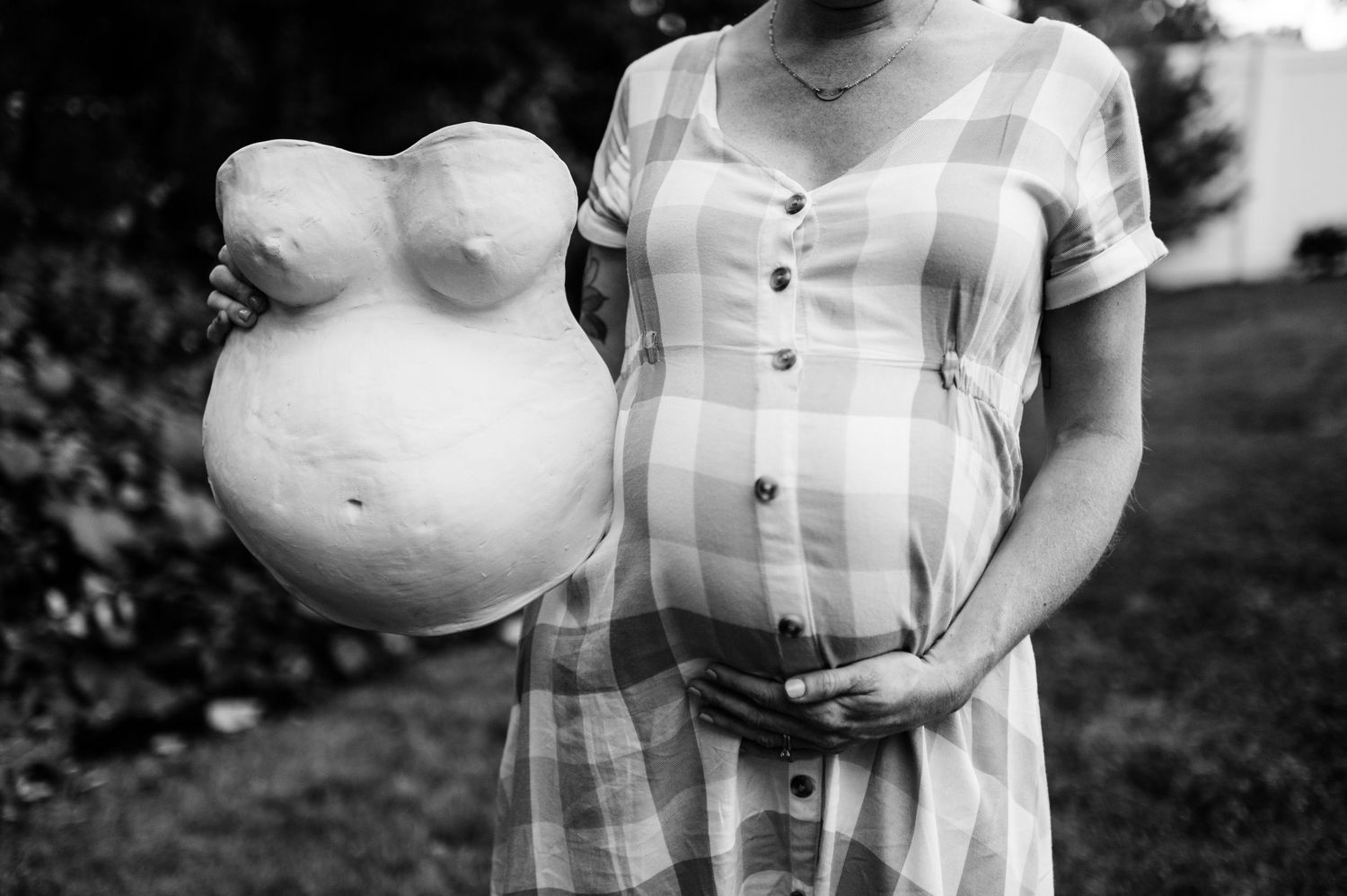A black and white maternity photo shows a couple embracing in a field with soft natural lighting.