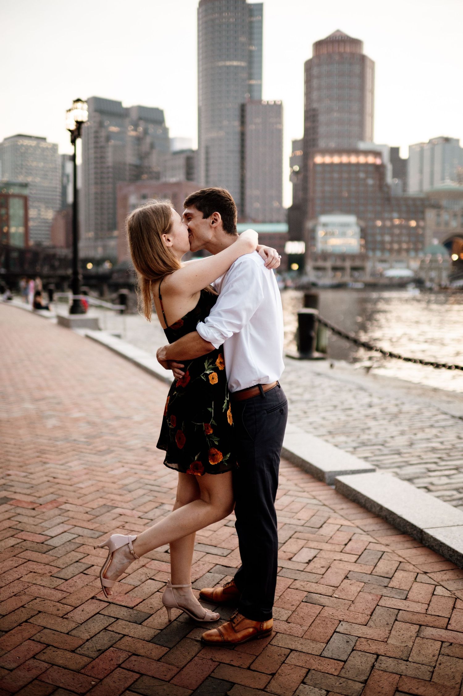 Couple shares romantic dip kiss against urban cityscape backdrop on brick paved walkway.