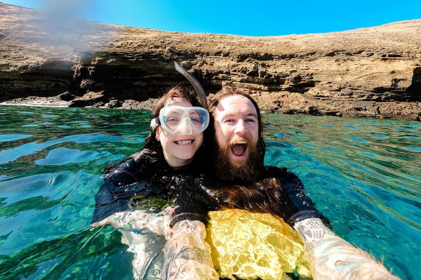 Swimmers snorkeling in crystal clear turquoise waters near rocky cliffs on a sunny Mediterranean day.