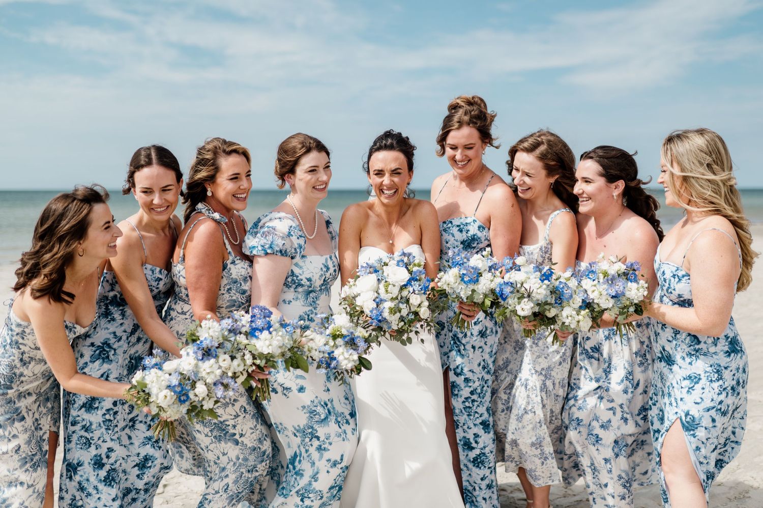 Bridesmaids in matching blue floral dresses laughing together outdoors.