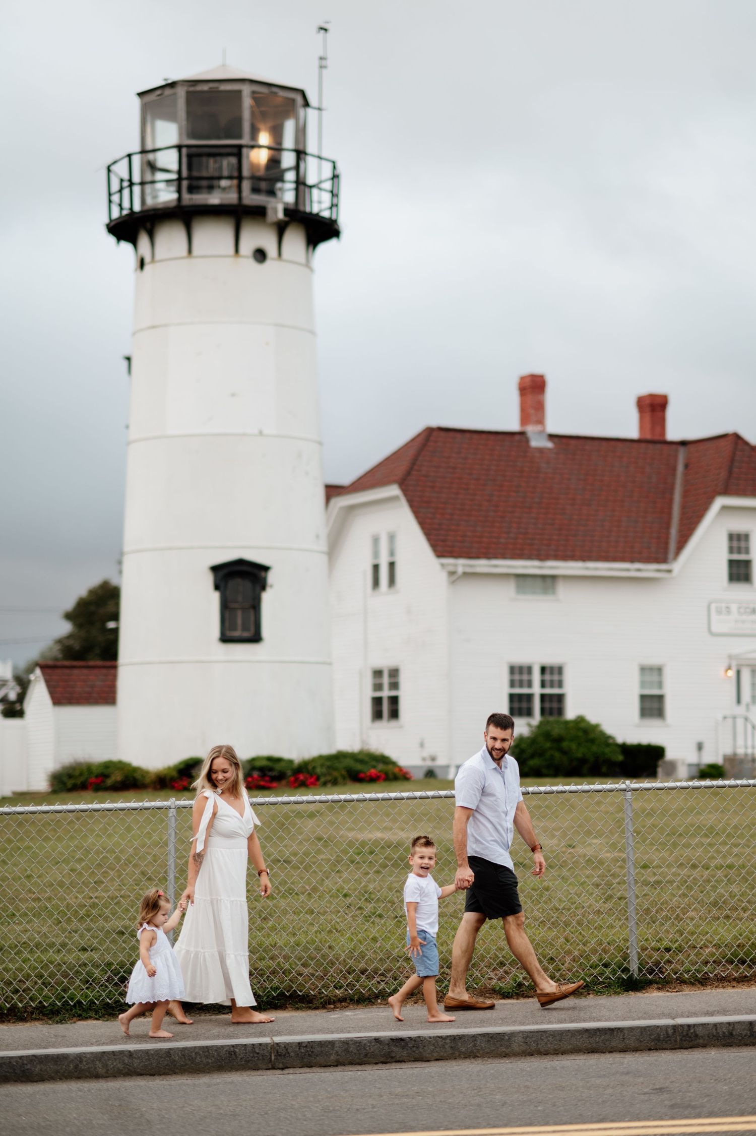A sequence showing people walking past a white lighthouse with red-roofed buildings.