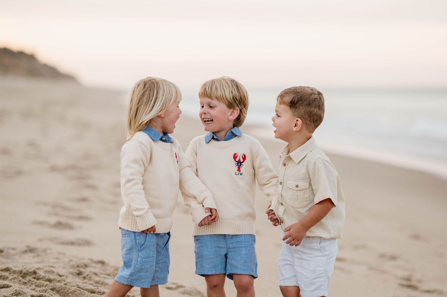 Children in coordinating light blue and white outfits play together on a sandy beach at sunset.