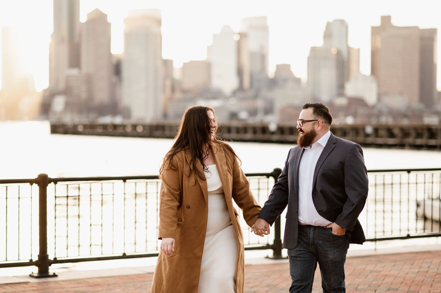 Couple shares intimate moments along city waterfront during golden hour engagement photoshoot.
