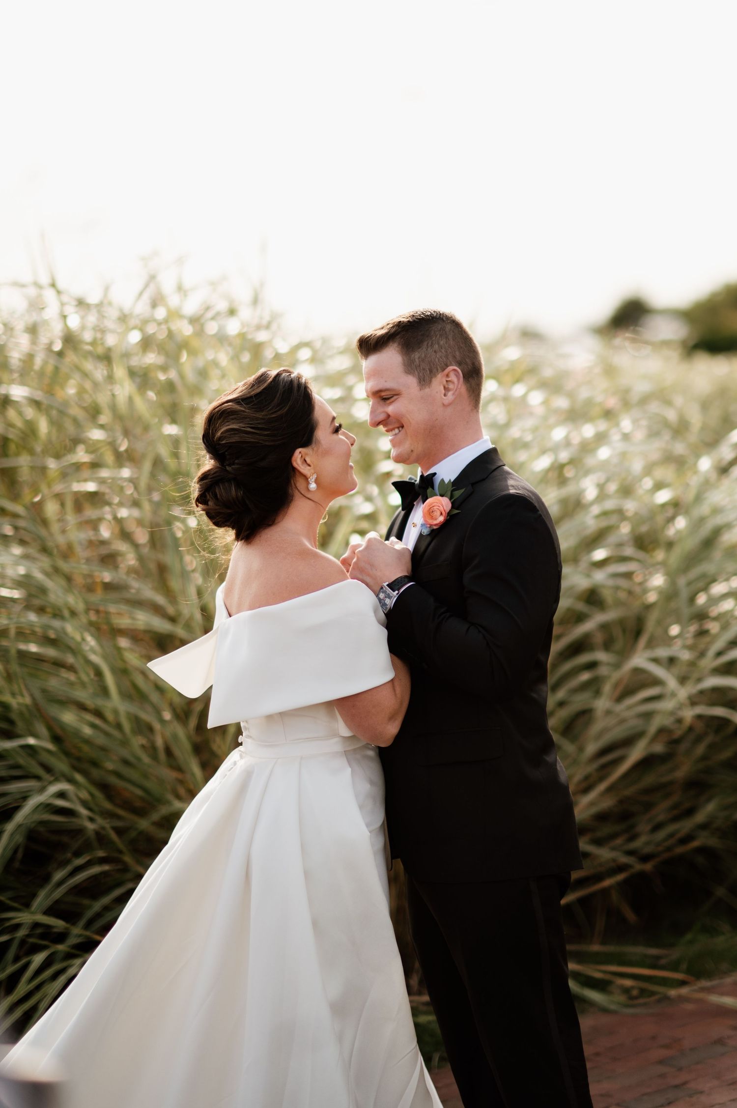 A romantic wedding couple shares tender moments together in front of blooming ornamental grasses at sunset.