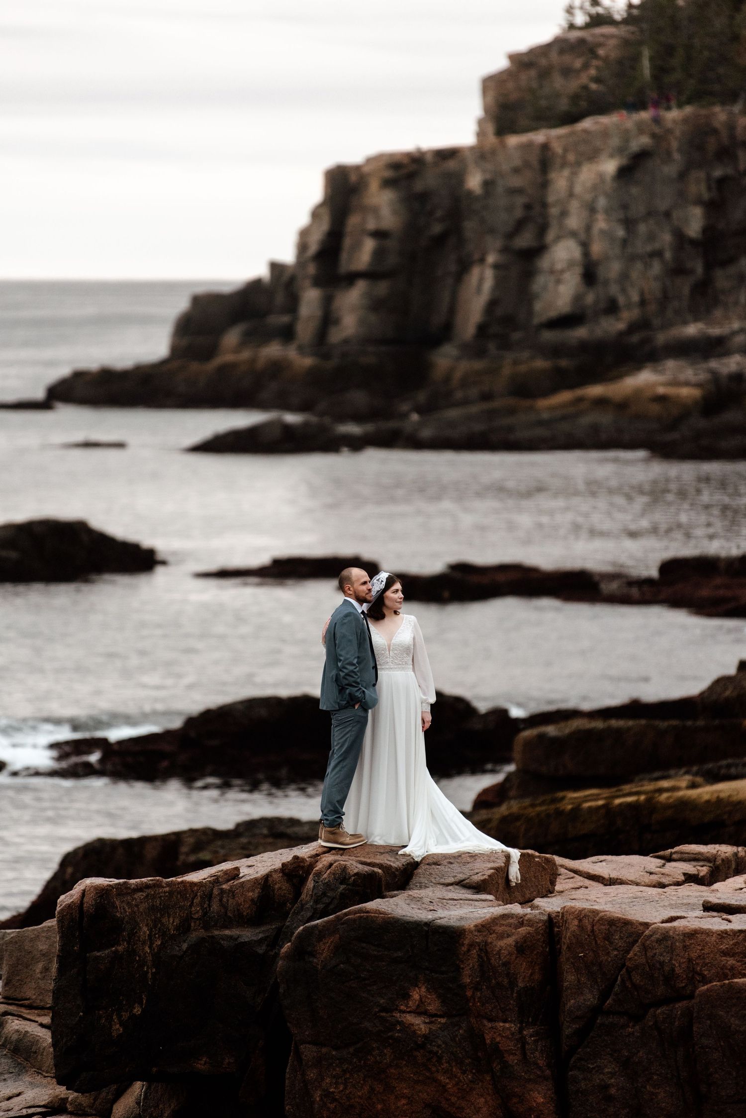 Couple stands on dramatic rocky coastal cliffs for romantic wedding portrait.