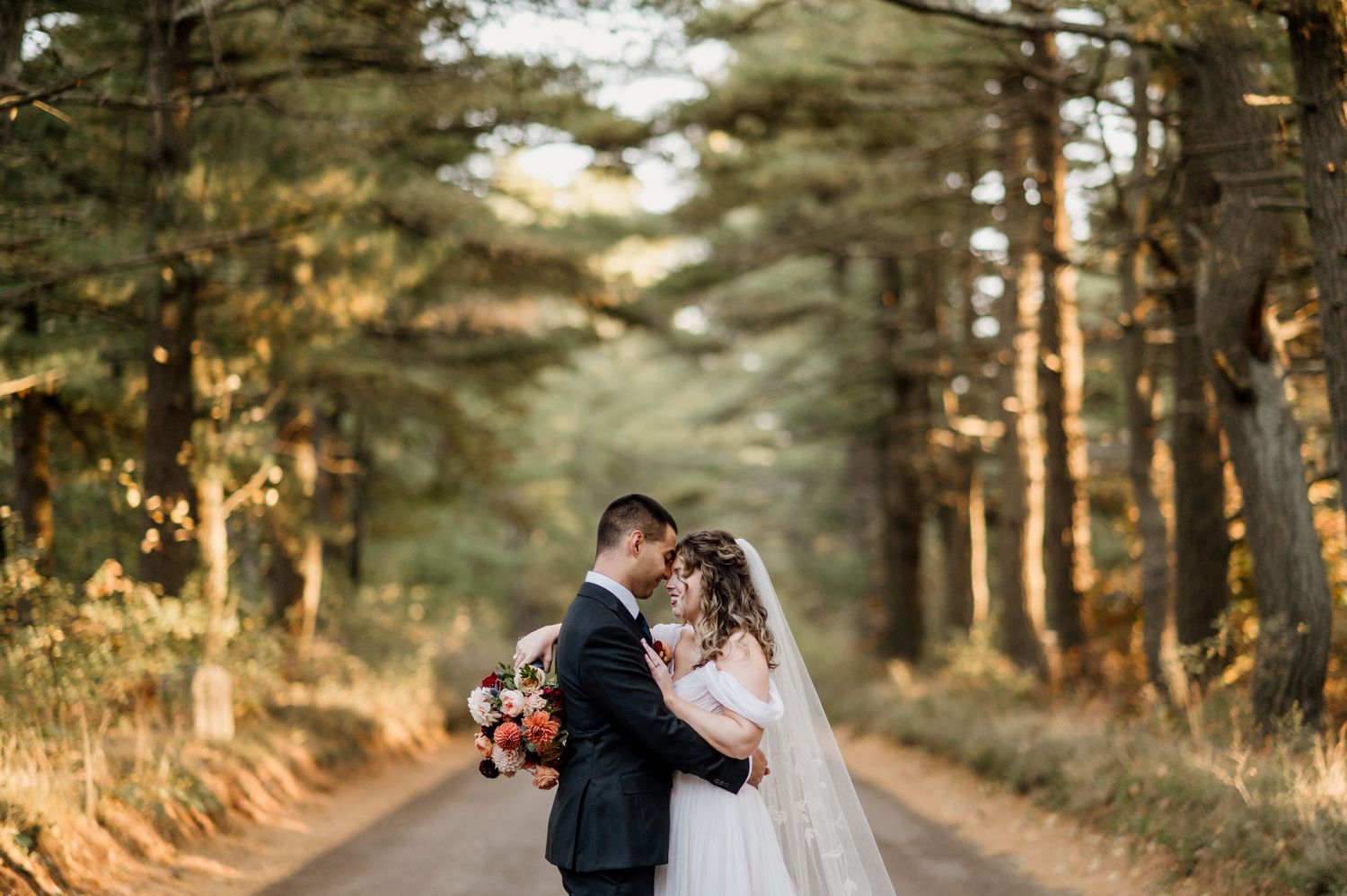 Romantic wedding couple embraces on a tree-lined path during golden hour sunset.