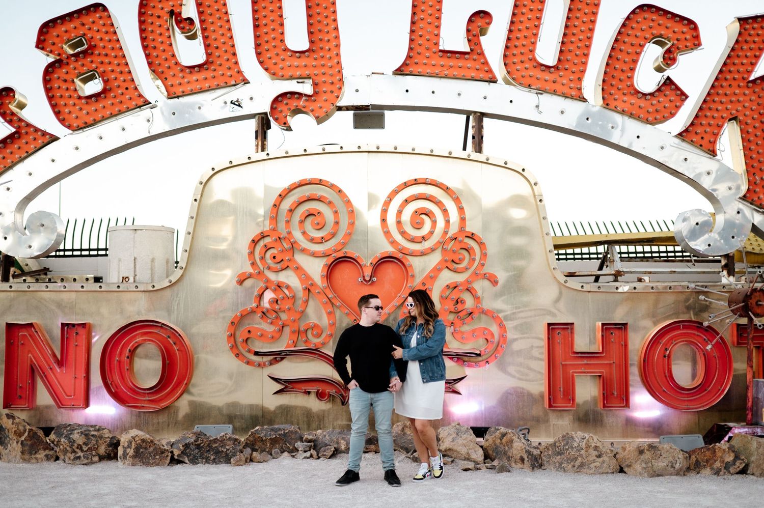 A couple poses against a vibrant orange and white graffiti wall with artistic swirls and text.