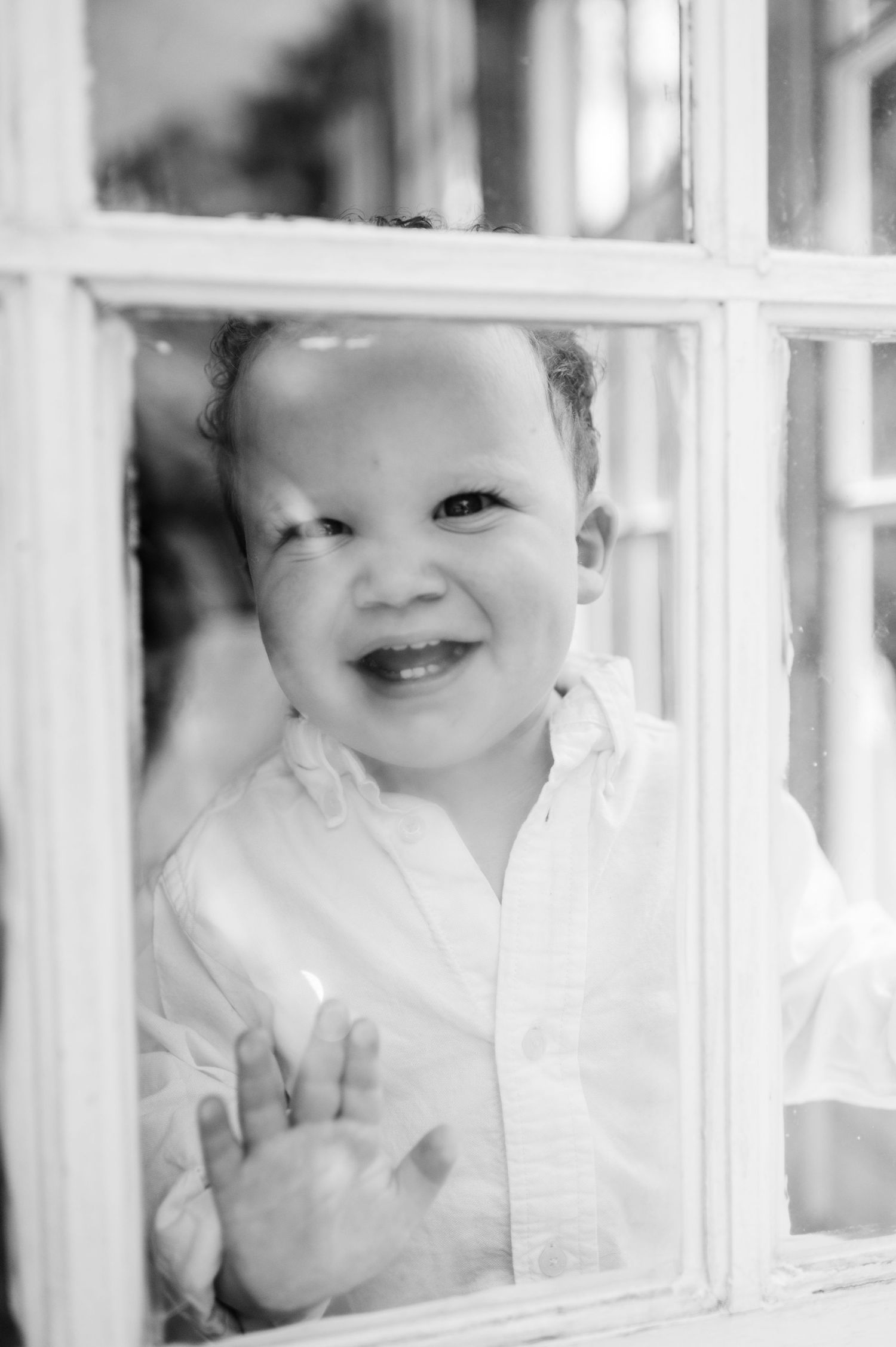 A baby peers through white window panes with a playful expression.