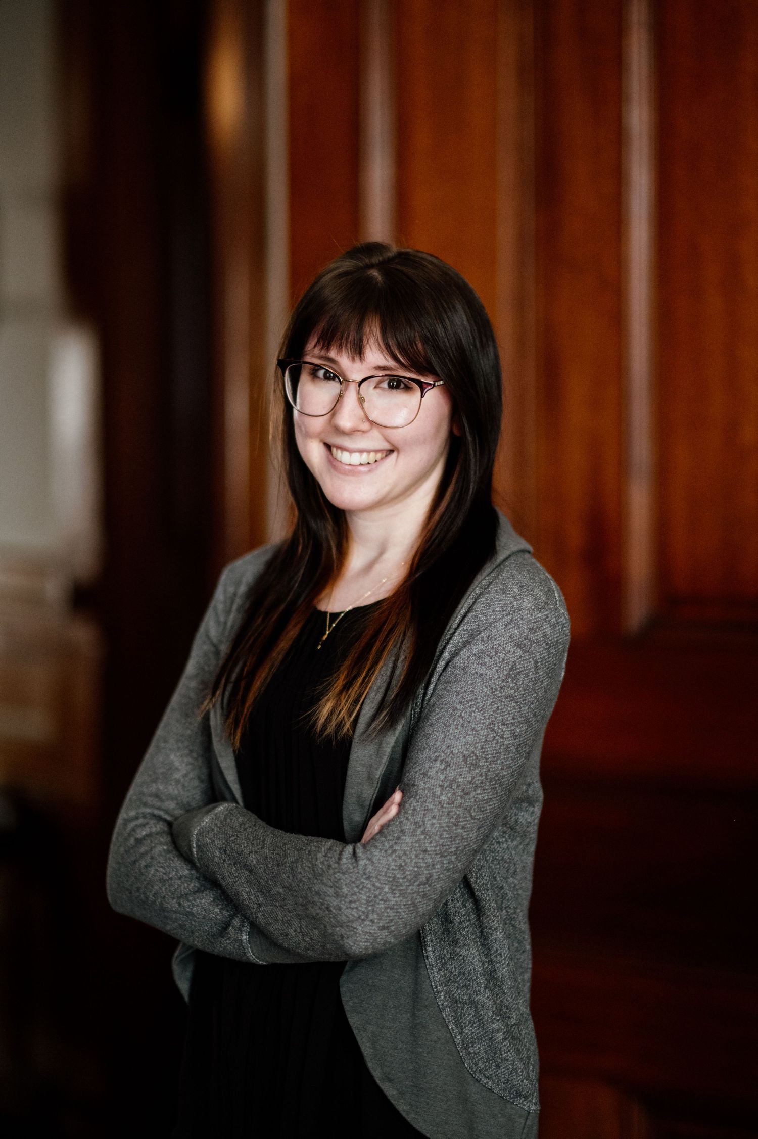 Professional indoor portrait series featuring a grey cardigan and glasses against a dark wood paneled background.