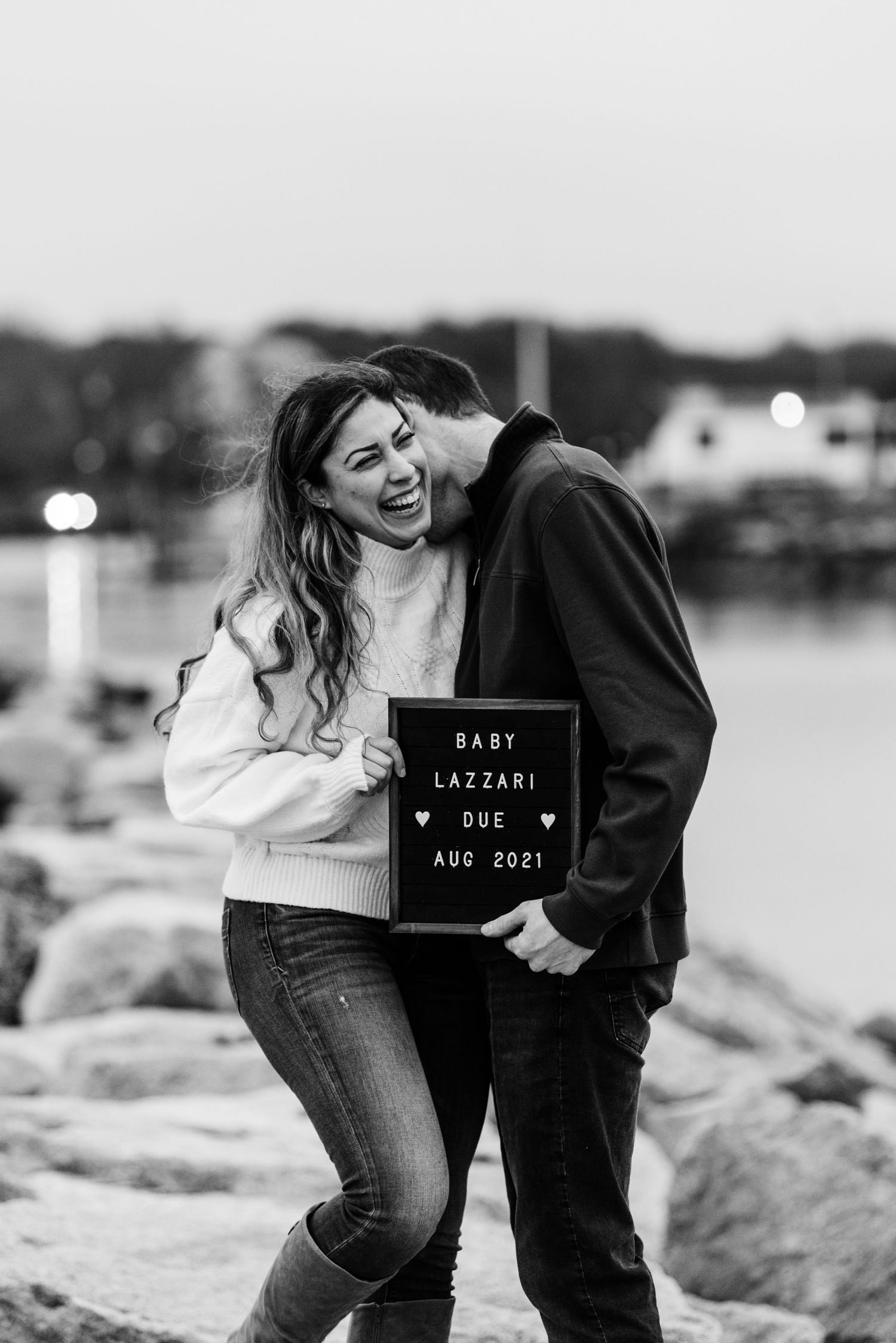 Black and white pregnancy announcement photos with letterboard signs on rocky beach.