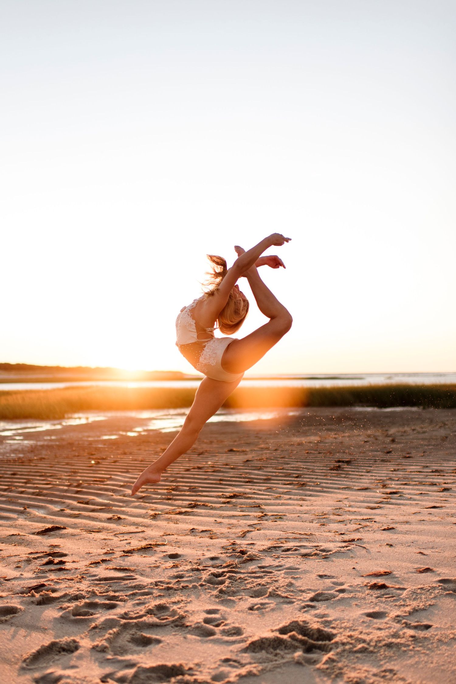 Dancer leaping gracefully on beach at sunset with golden light illuminating the sand.
