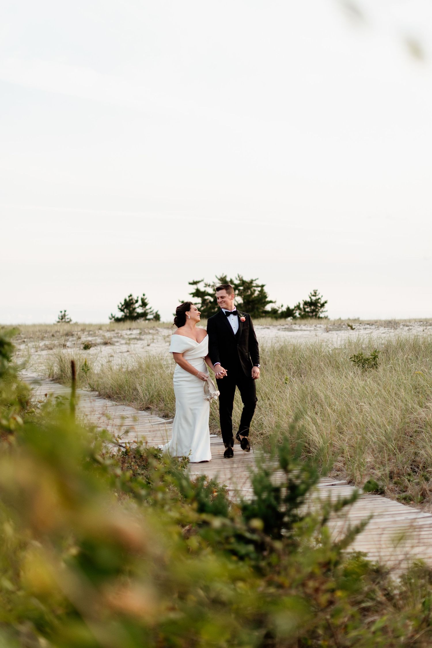 Couple walking along a sandy beach boardwalk surrounded by beach grass and dunes.