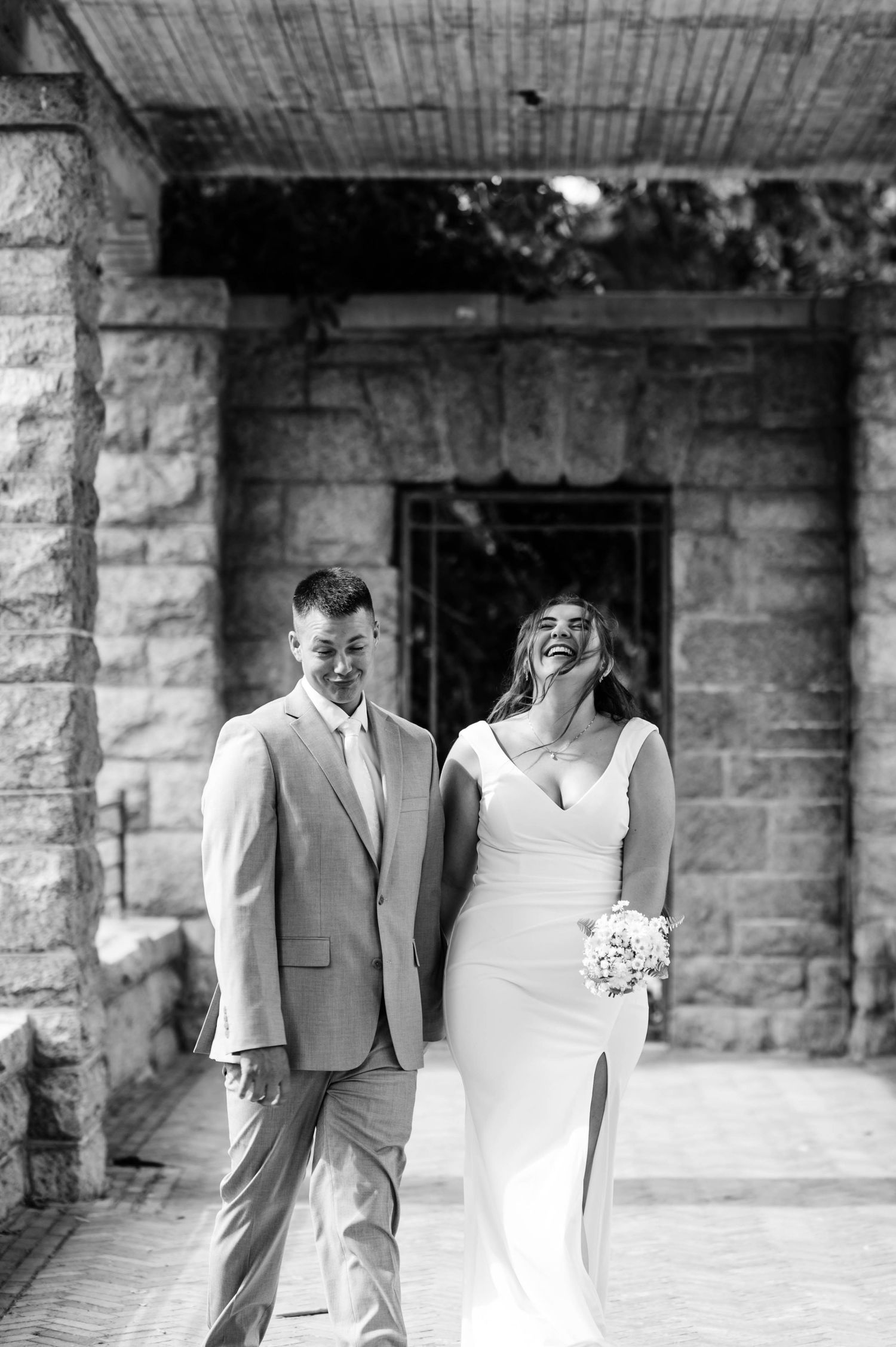 A joyful wedding couple shares a candid moment together on a stone porch in black and white.