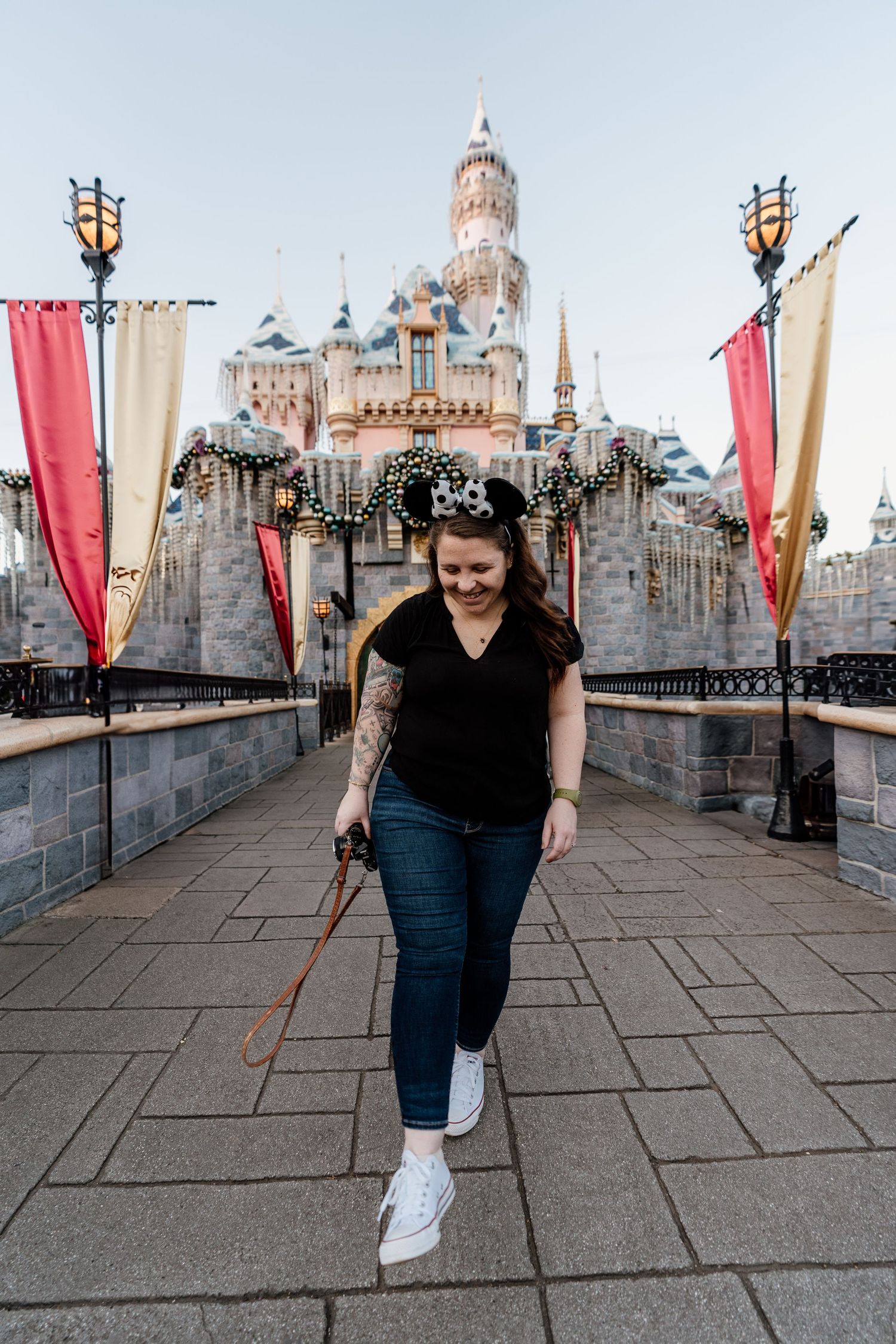 Visitor walks along castle pathway with red banners and Sleeping Beauty Castle decorated for holidays at Disneyland.