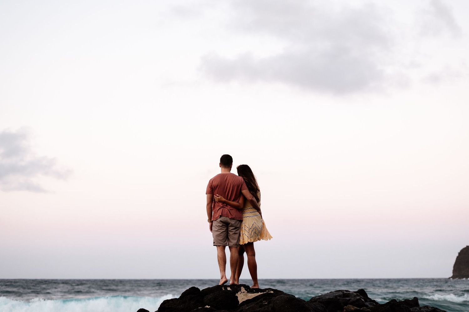 Silhouettes of a couple walking along a scenic beach at dusk.