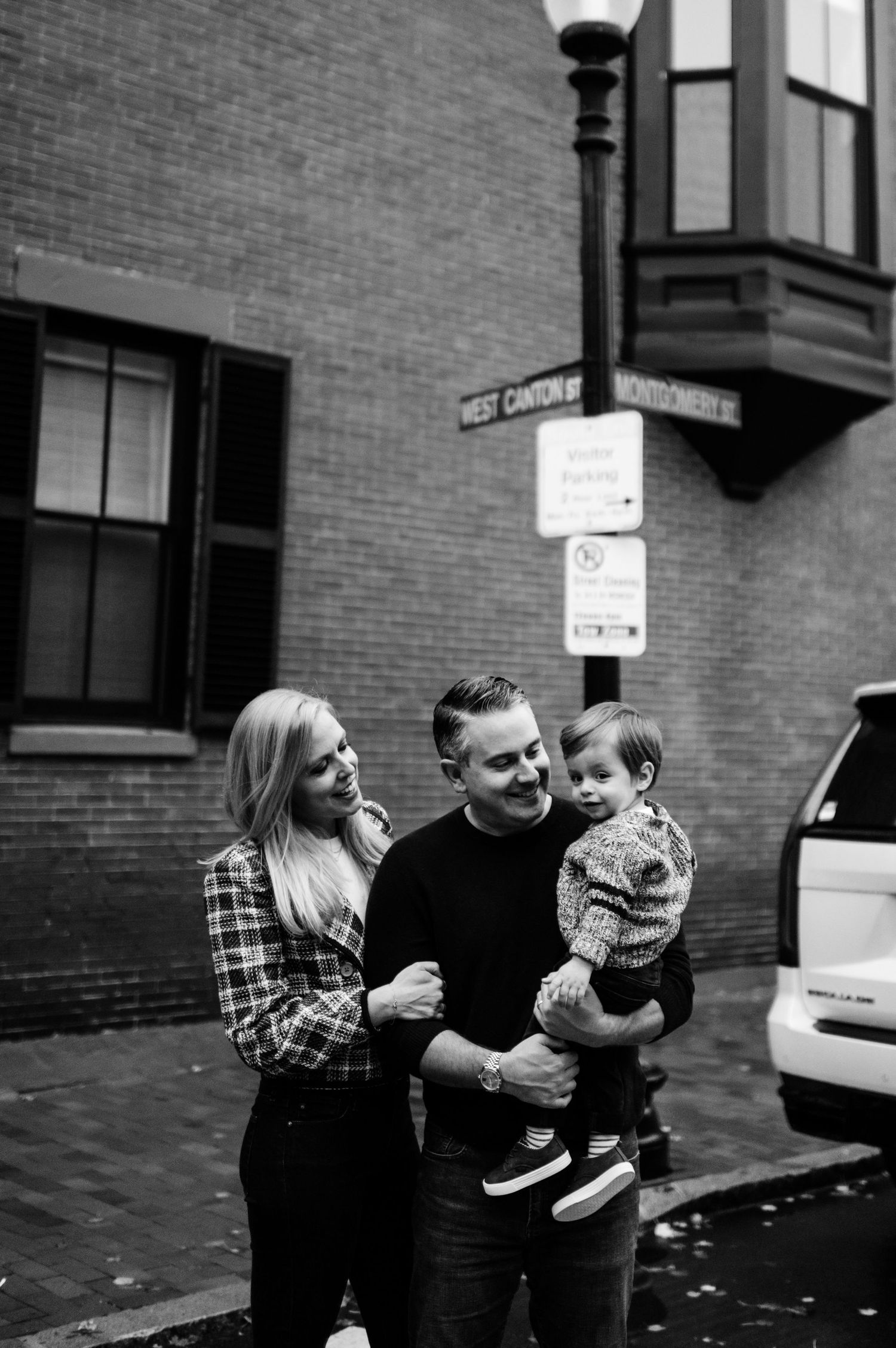 Black and white photo of a family moment outside a brick building in an urban setting.