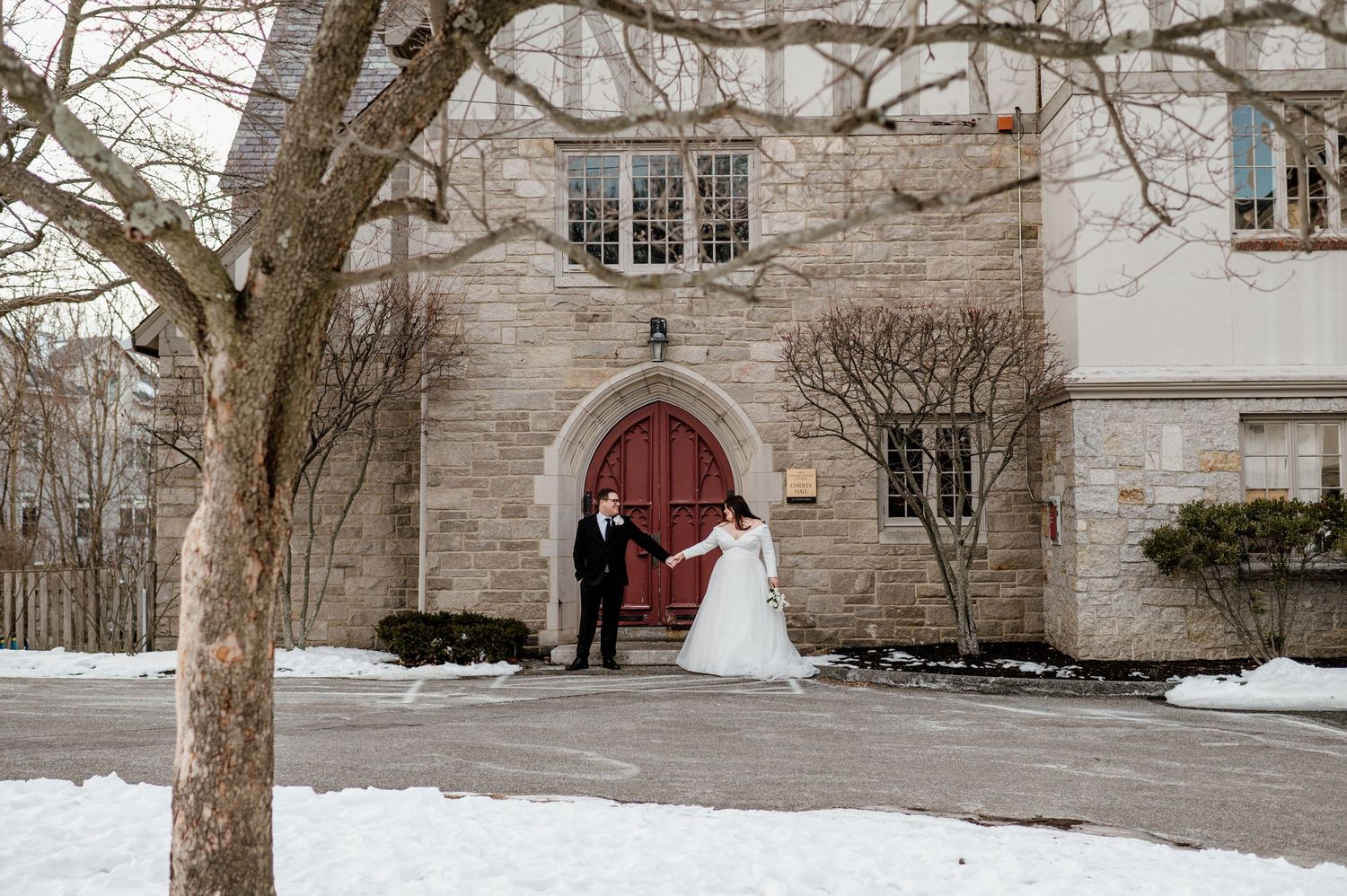 Stone church exterior with red door and snow covered grounds in winter setting.