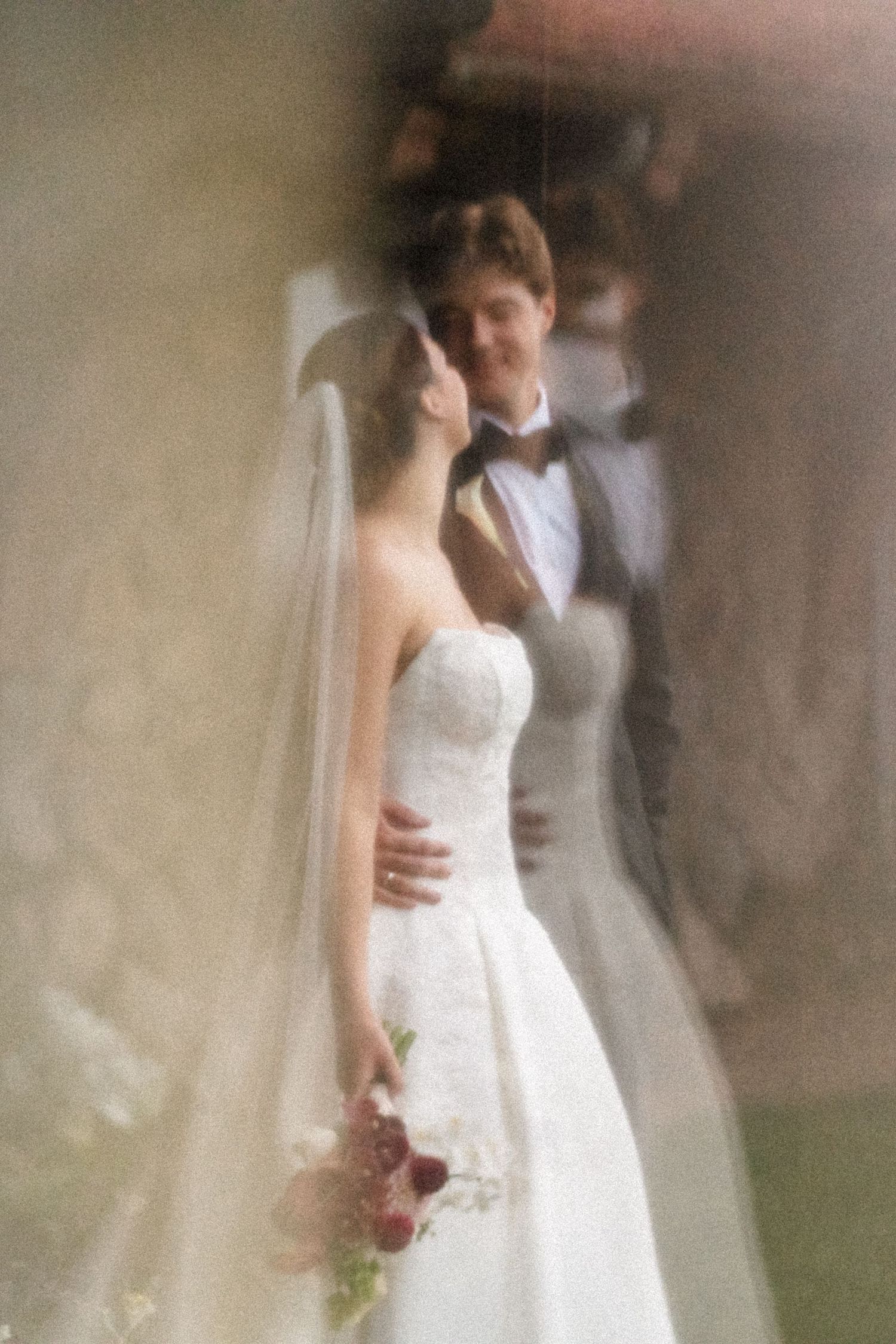 Bride in white strapless gown holding bouquet with groom in tuxedo sharing romantic moment at wedding ceremony.