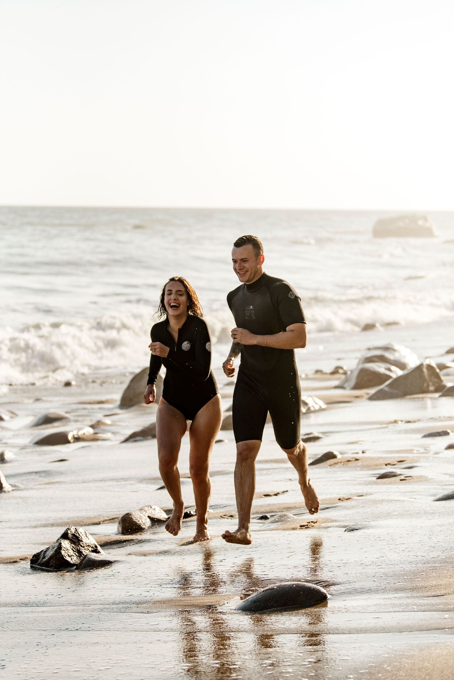 Couple playing and running along beach shoreline at sunset with waves crashing nearby.