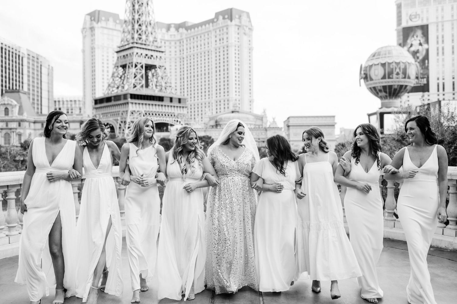 A group of people wearing traditional white graduation gowns walk in a procession line during a ceremony.
