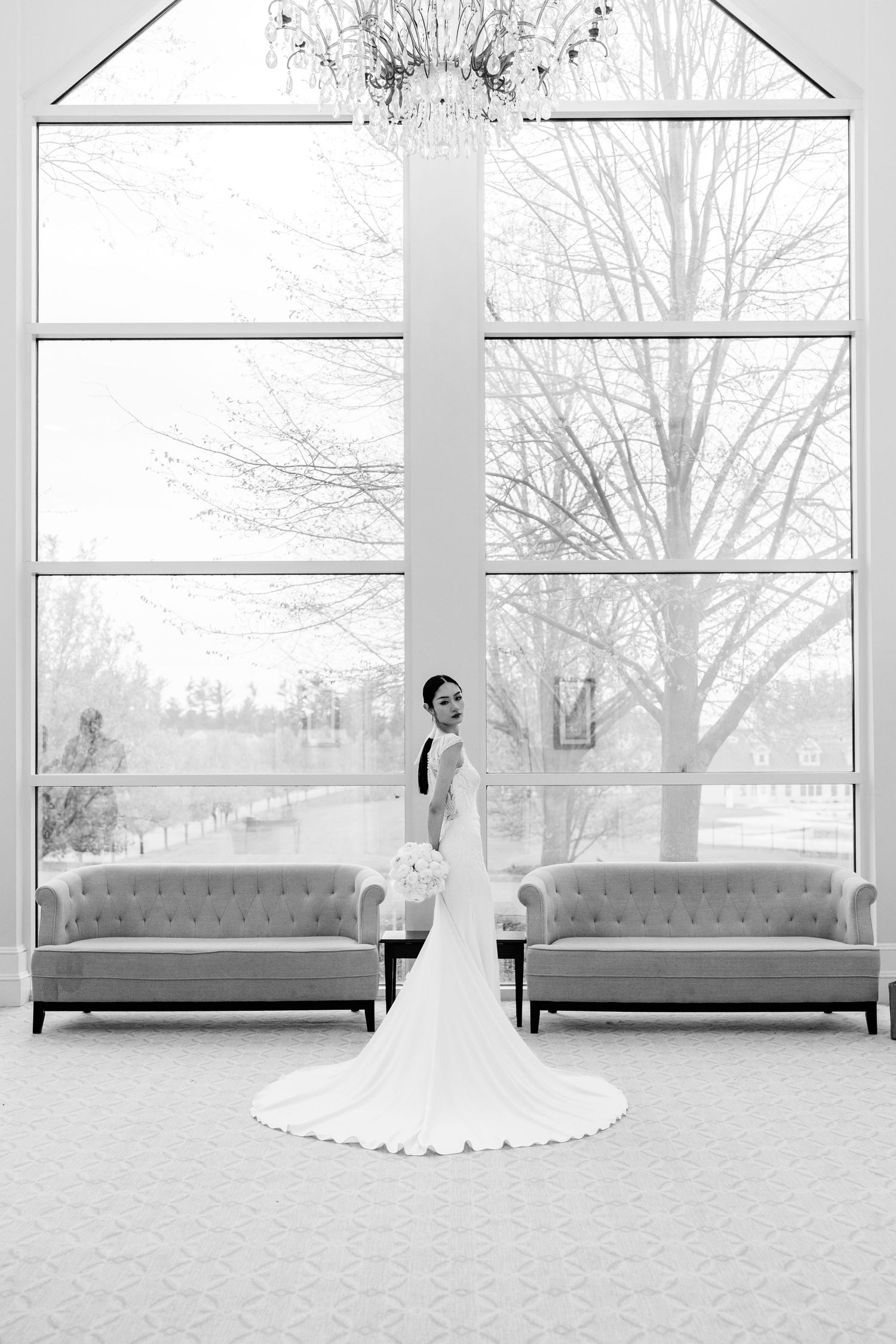 A minimalist bridal portrait series in black and white featuring a flowing white gown against large windows.