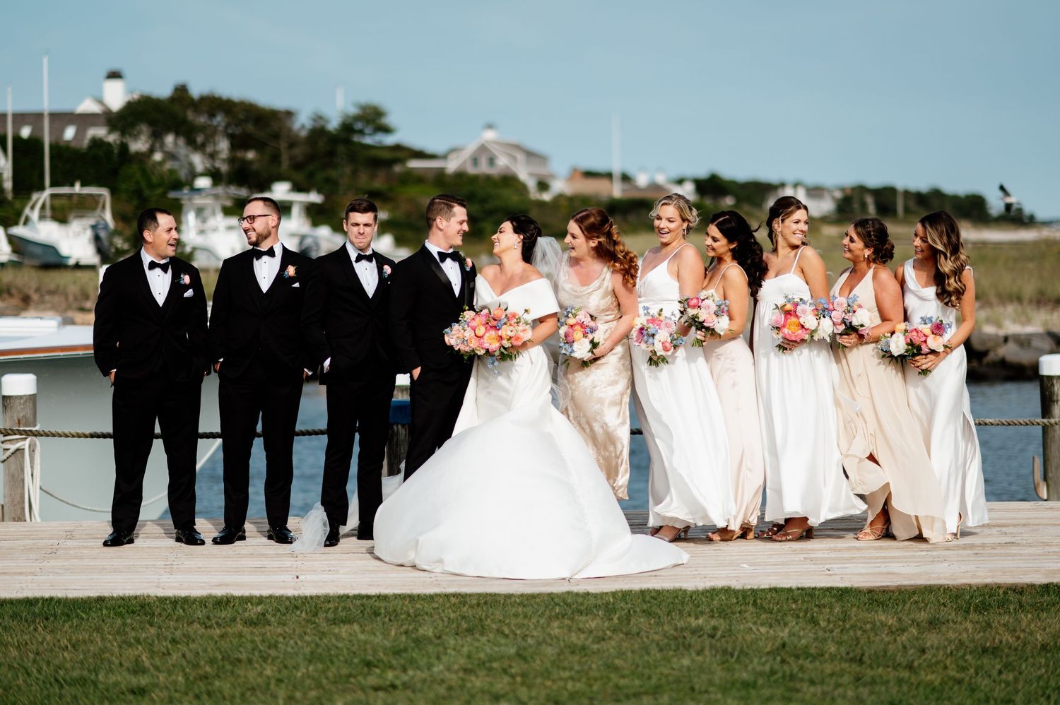 Wedding party portrait at waterfront location with bridesmaids in white and groomsmen in dark suits.
