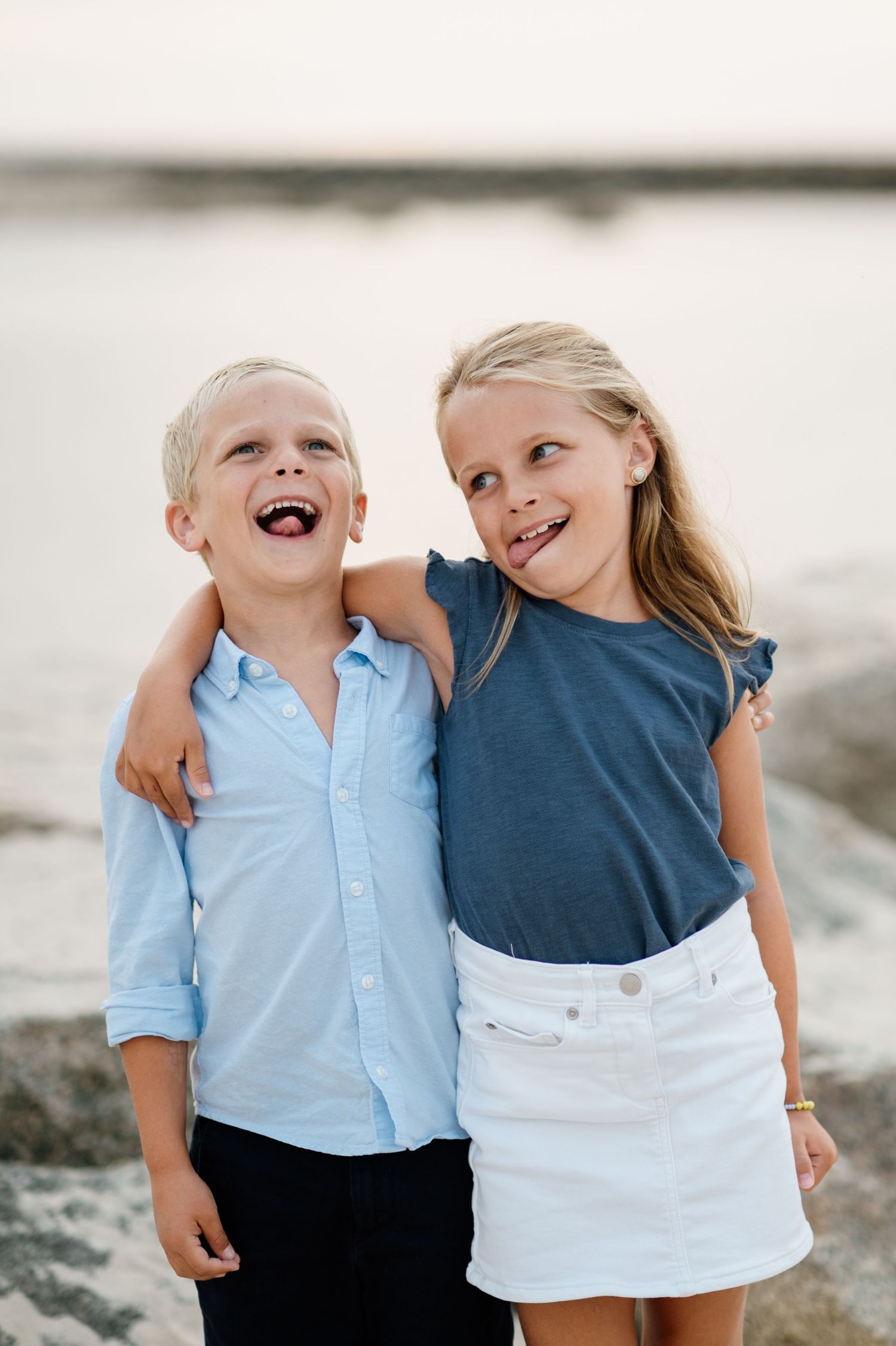 Two children in blue and white outfits sharing a playful moment by the water.