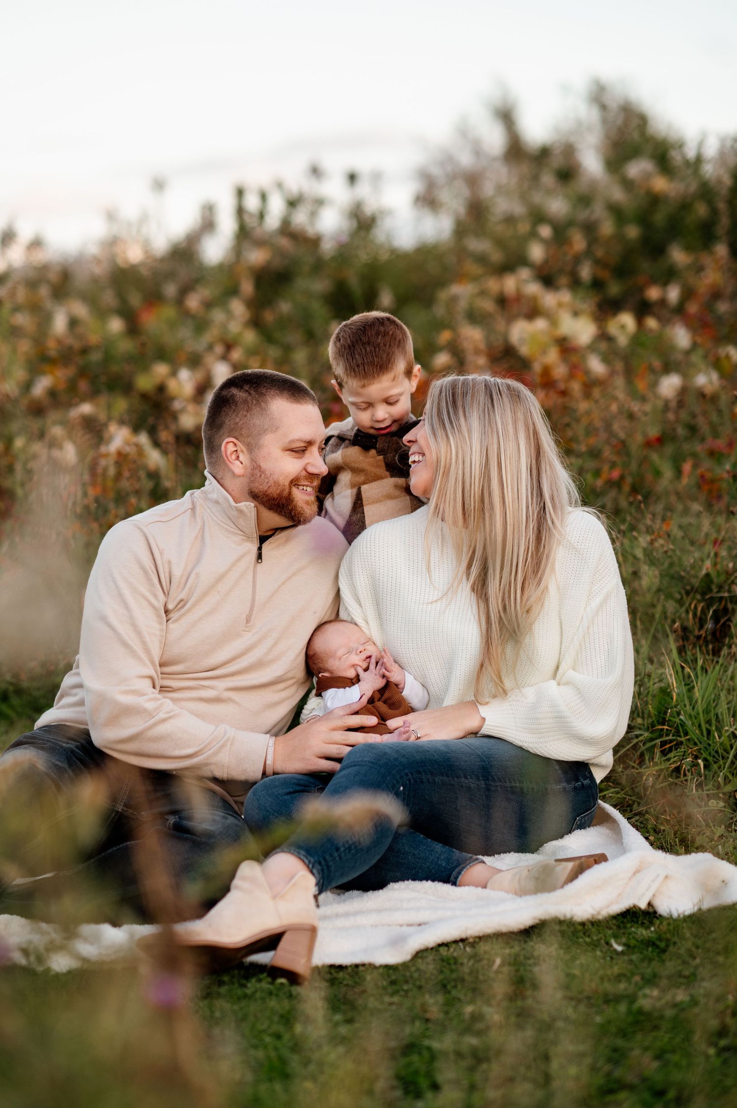Family sitting on blanket outdoors with newborn baby during golden hour.