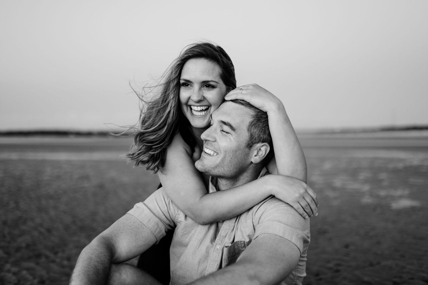 Romantic couple embracing in a scenic black and white beach landscape at sunset.