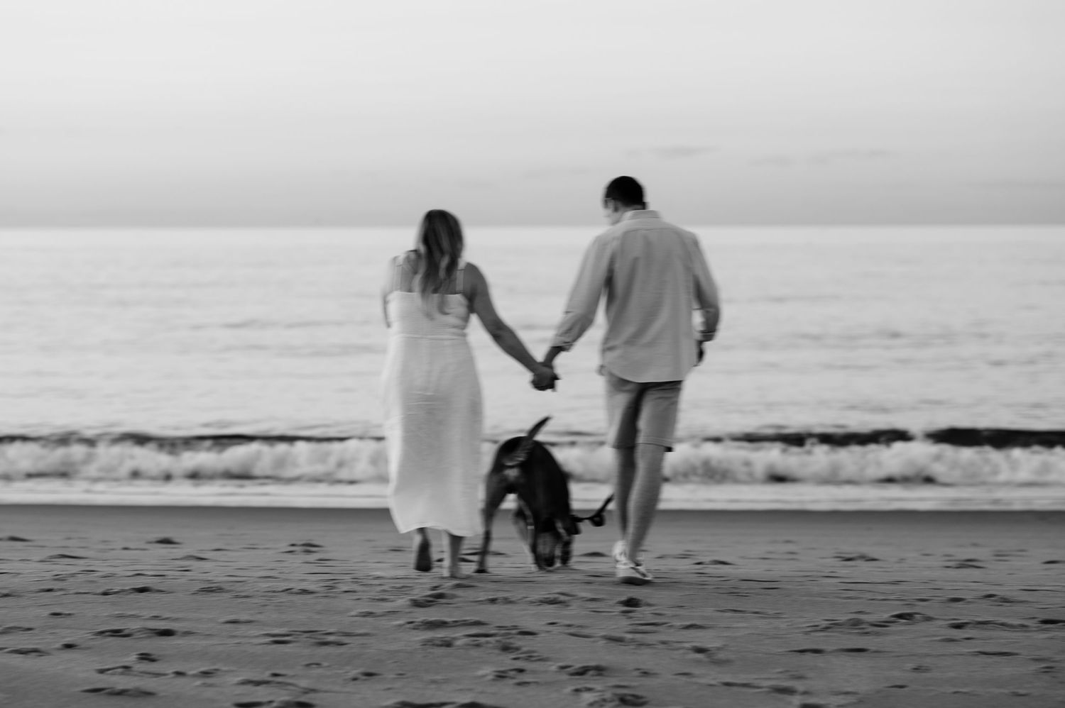 A silhouetted couple walks along a misty beach shoreline at dusk.
