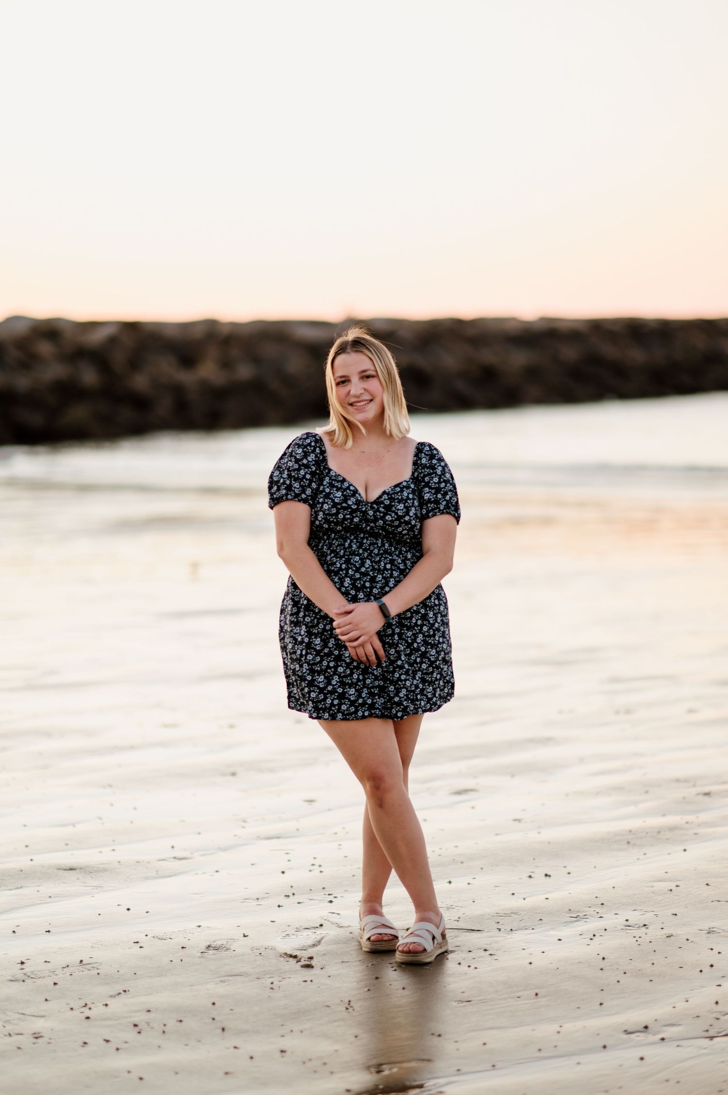 A person in a polka dot dress poses playfully on a sandy beach at sunset.