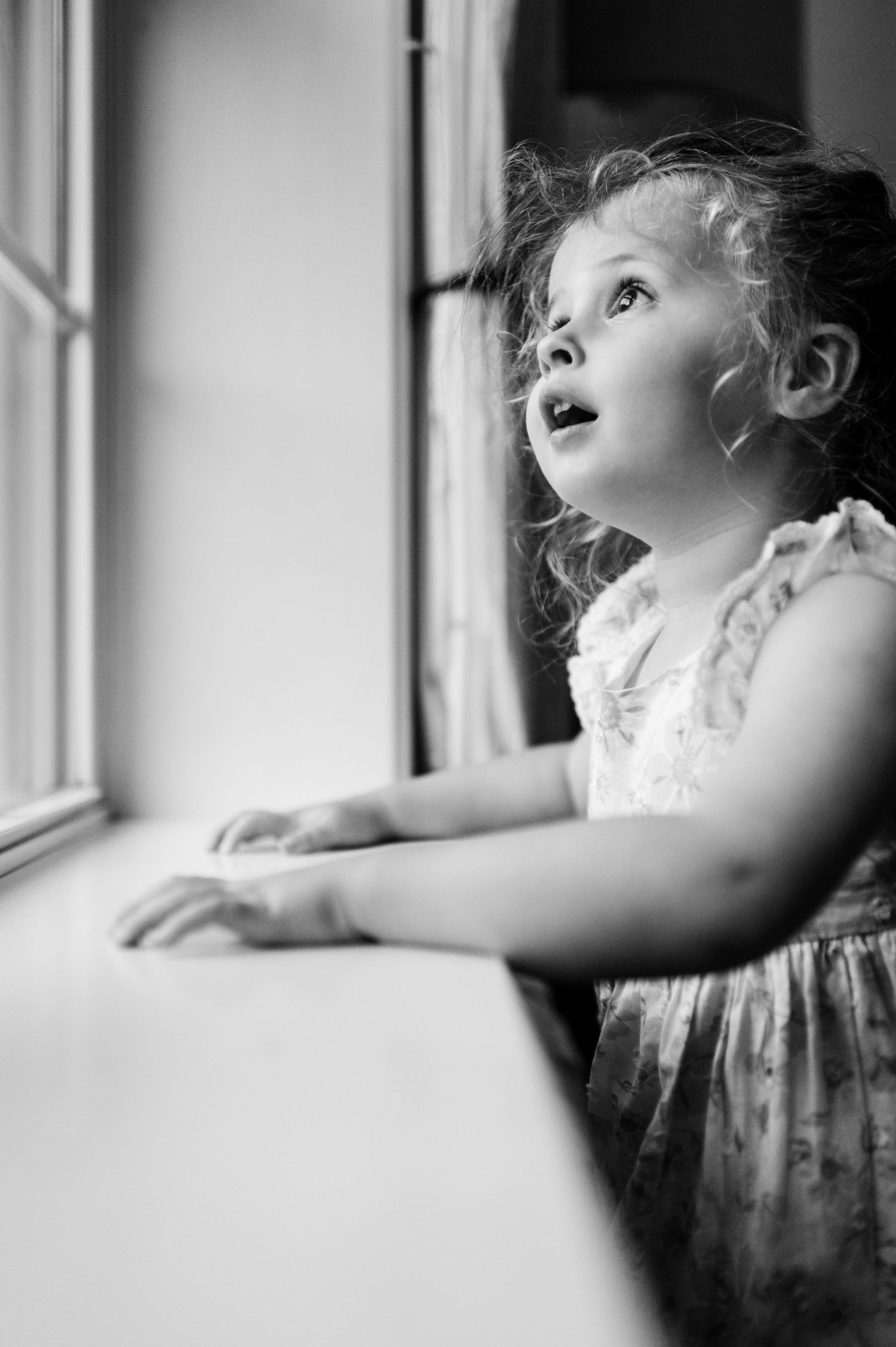 A series of black and white photographs showing a child gazing upward with wonder through a window.