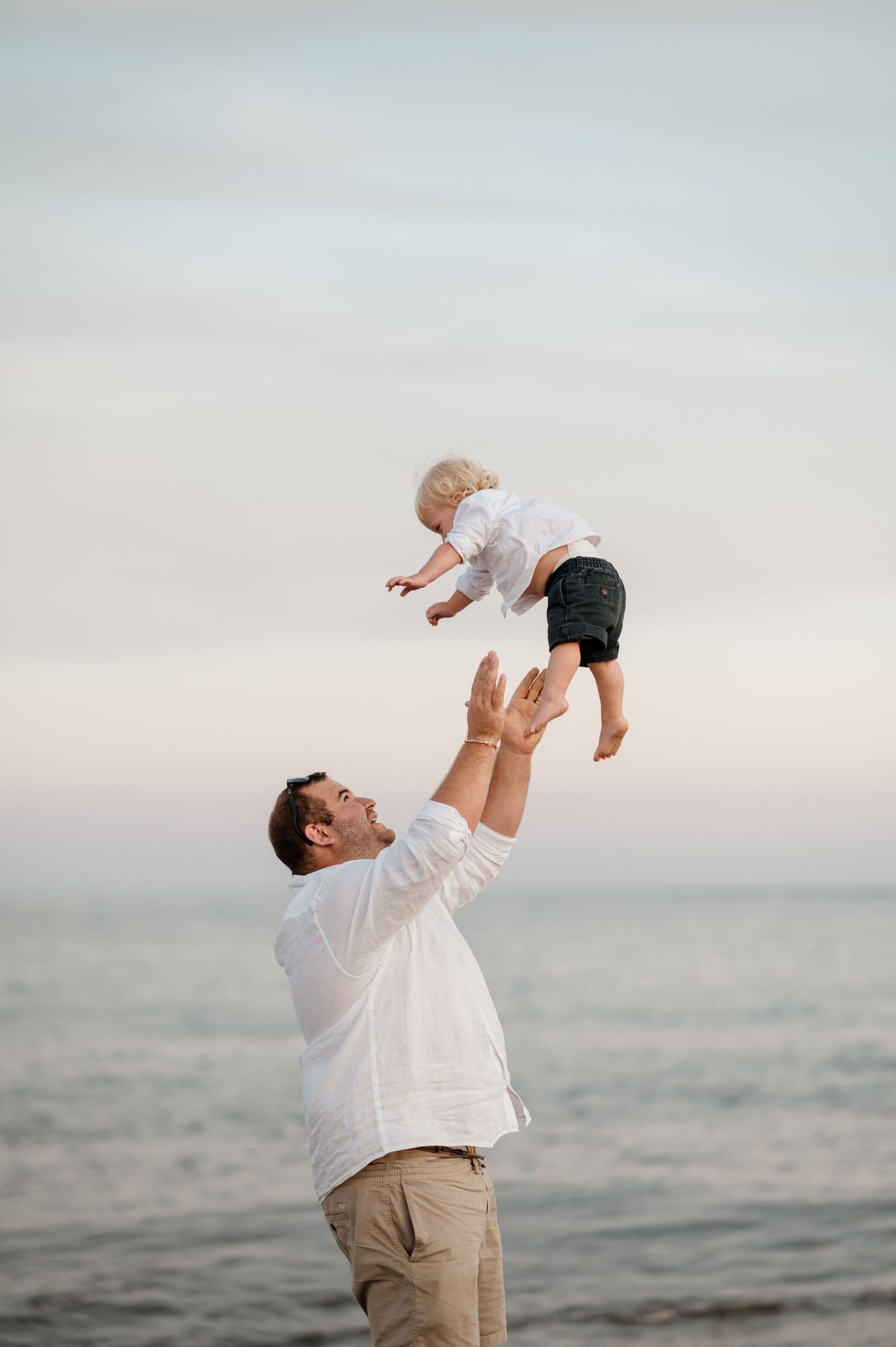 Heartwarming series of a parent tossing a baby in the air at the beach during sunset.