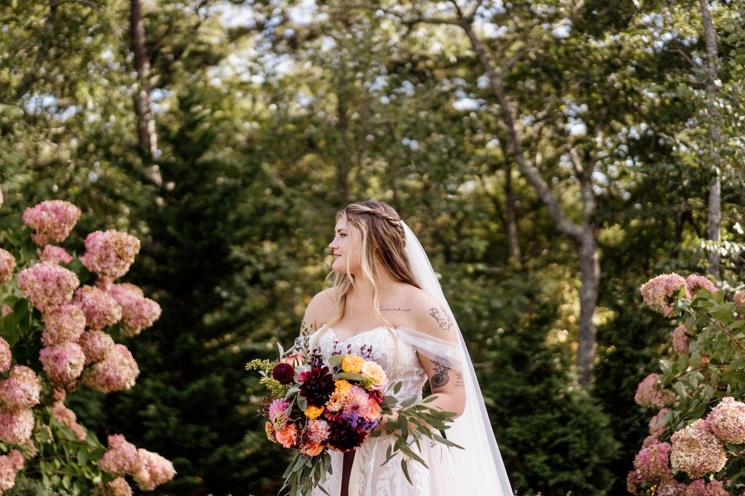 Wedding couple poses in garden with pink hydrangea flowers and greenery.