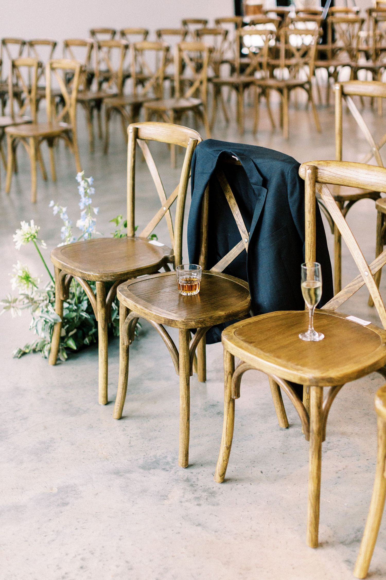 Rustic wooden crossback chairs arranged for wedding ceremony with delicate floral accents.
