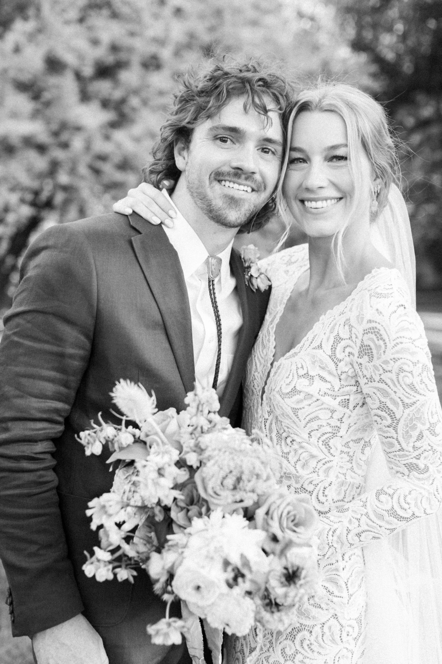 A romantic black and white wedding portrait showing a couple embracing with a beautiful floral bouquet.