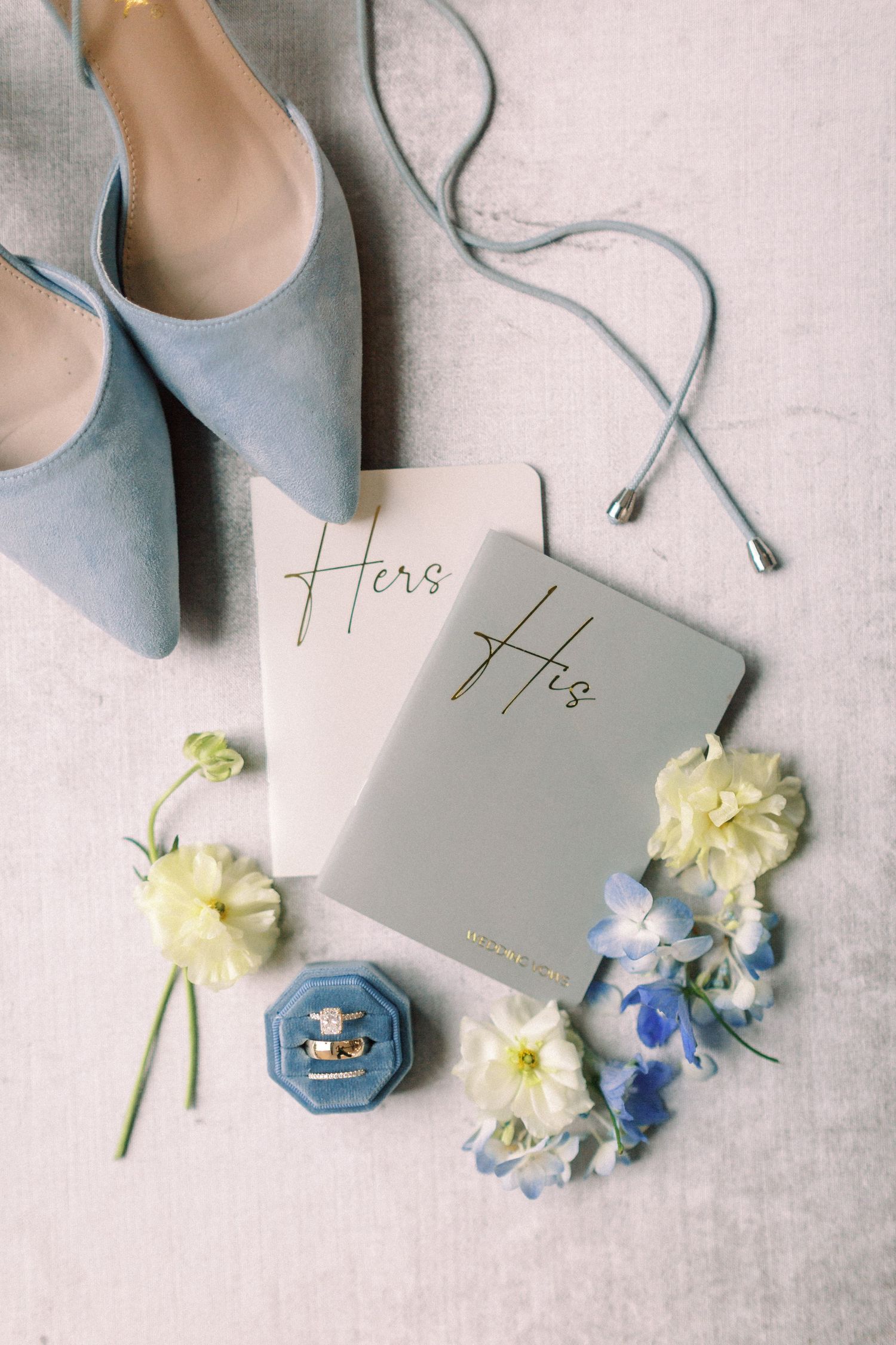 Wedding flat lay featuring blue shoes, invitation cards, and yellow and blue flowers.
