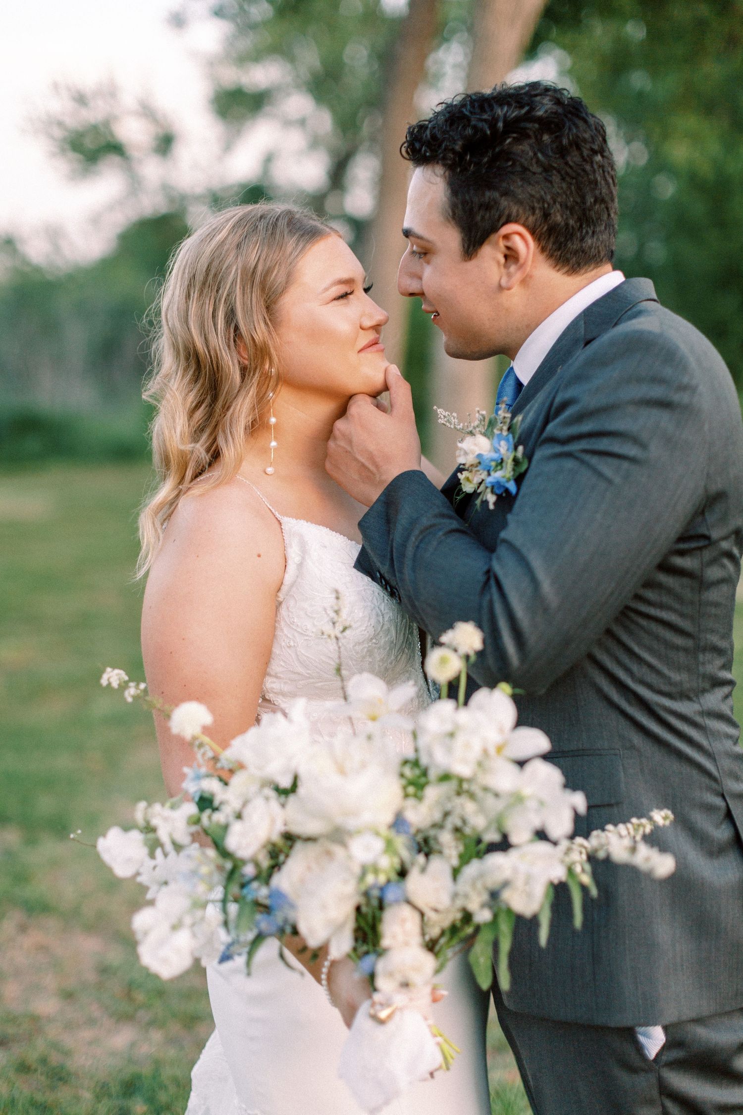Romantic wedding couple sharing intimate moments with white floral bouquet in garden setting.