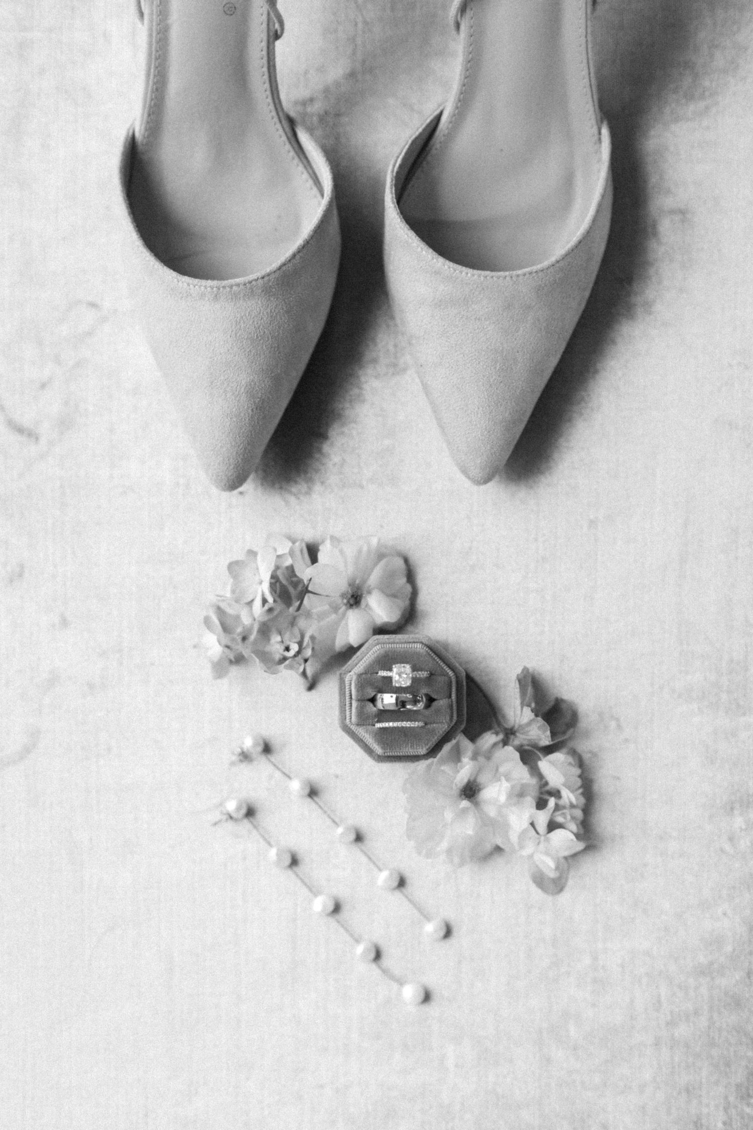 Wedding accessories including nude heels and delicate floral details arranged on a light gray background.