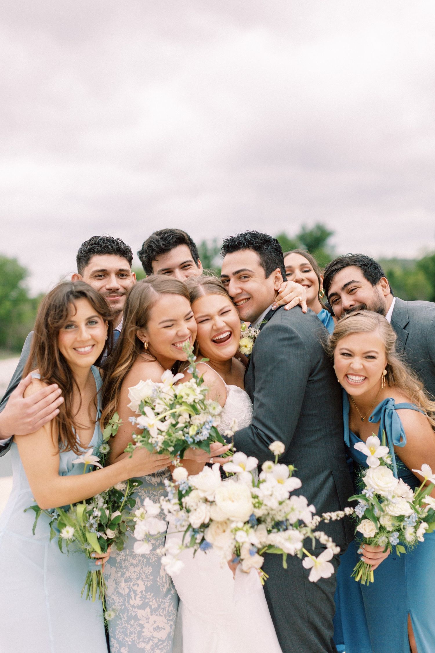 Wedding party in blue dresses and suits posing together with white floral bouquets.