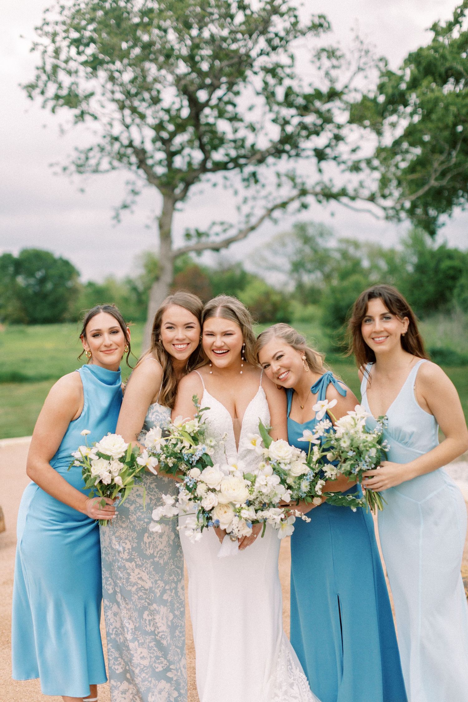 Wedding party in coordinating blue dresses gather close for a cheerful outdoor photo.