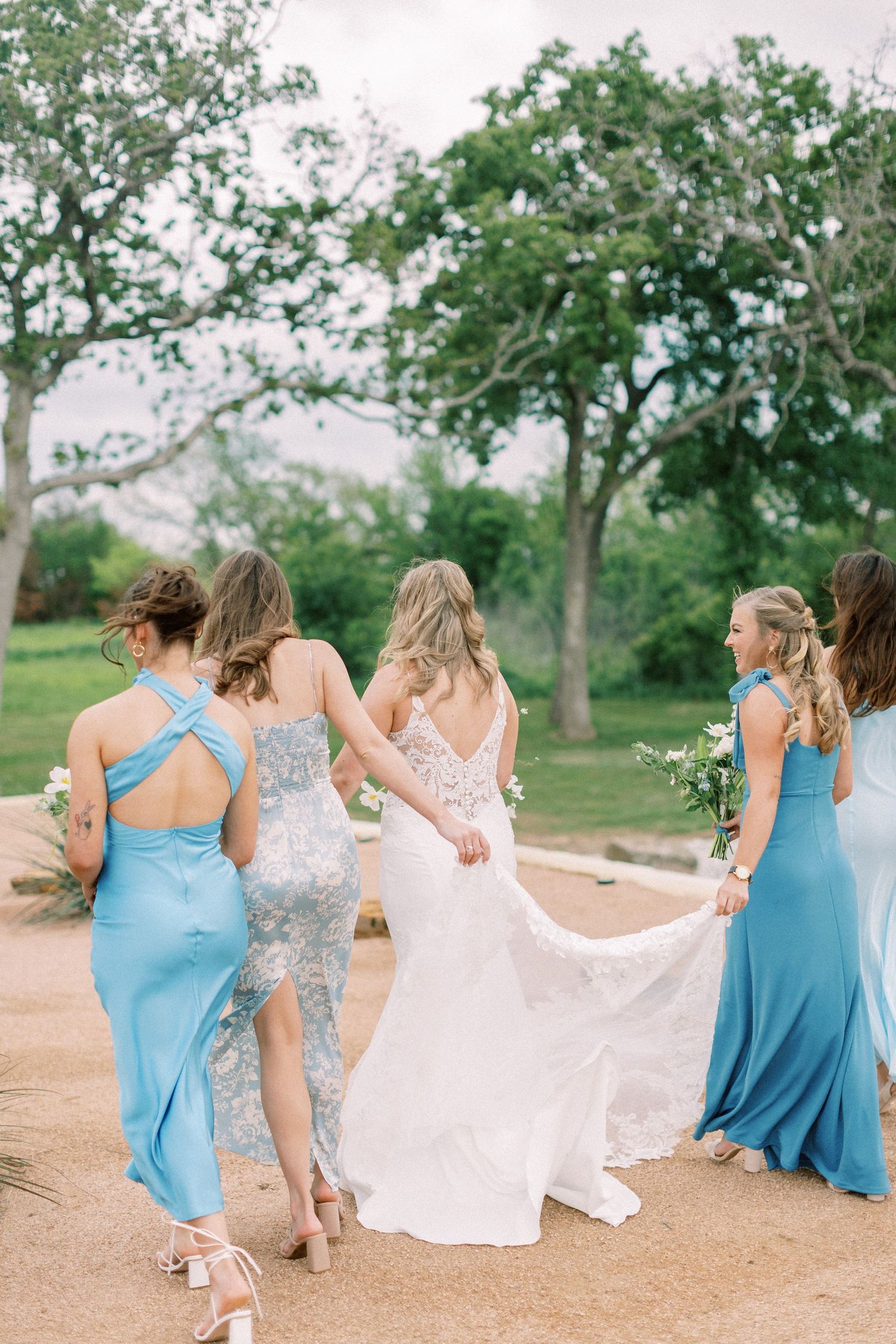 Back view of bridesmaids in blue dresses walking together outdoors.